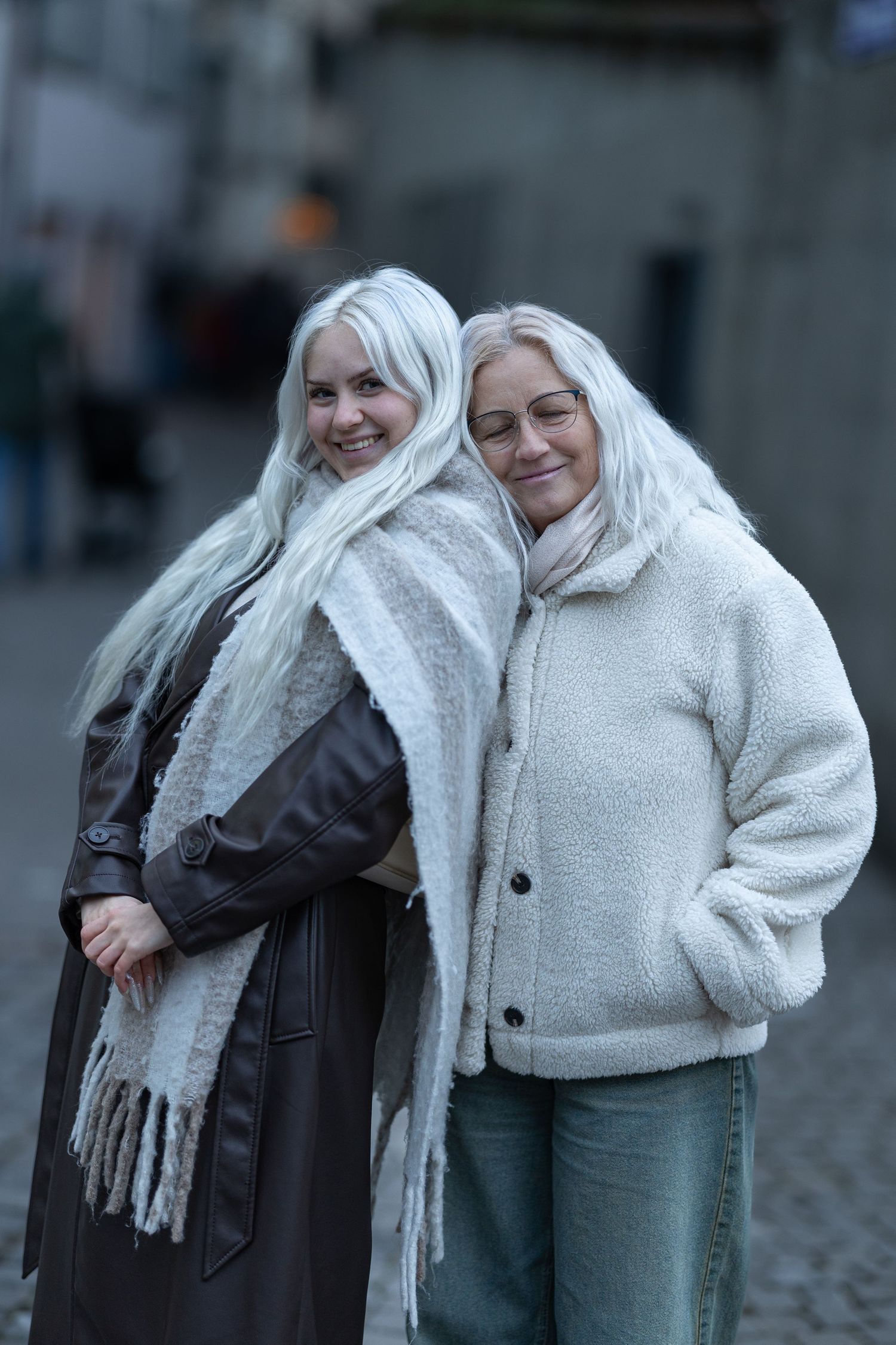 Two friends in white winter coats and scarves sharing a joyful moment outdoors.