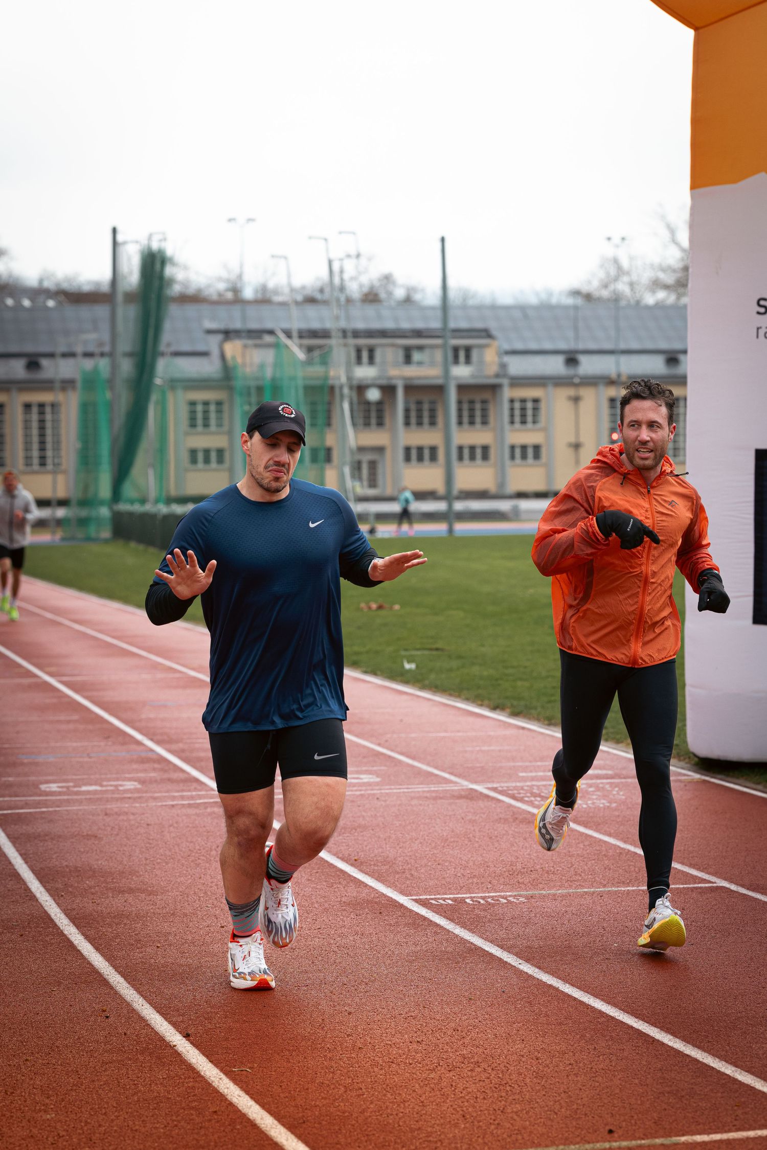 Athletes practicing sprint technique on an outdoor running track in orange and navy sportswear.