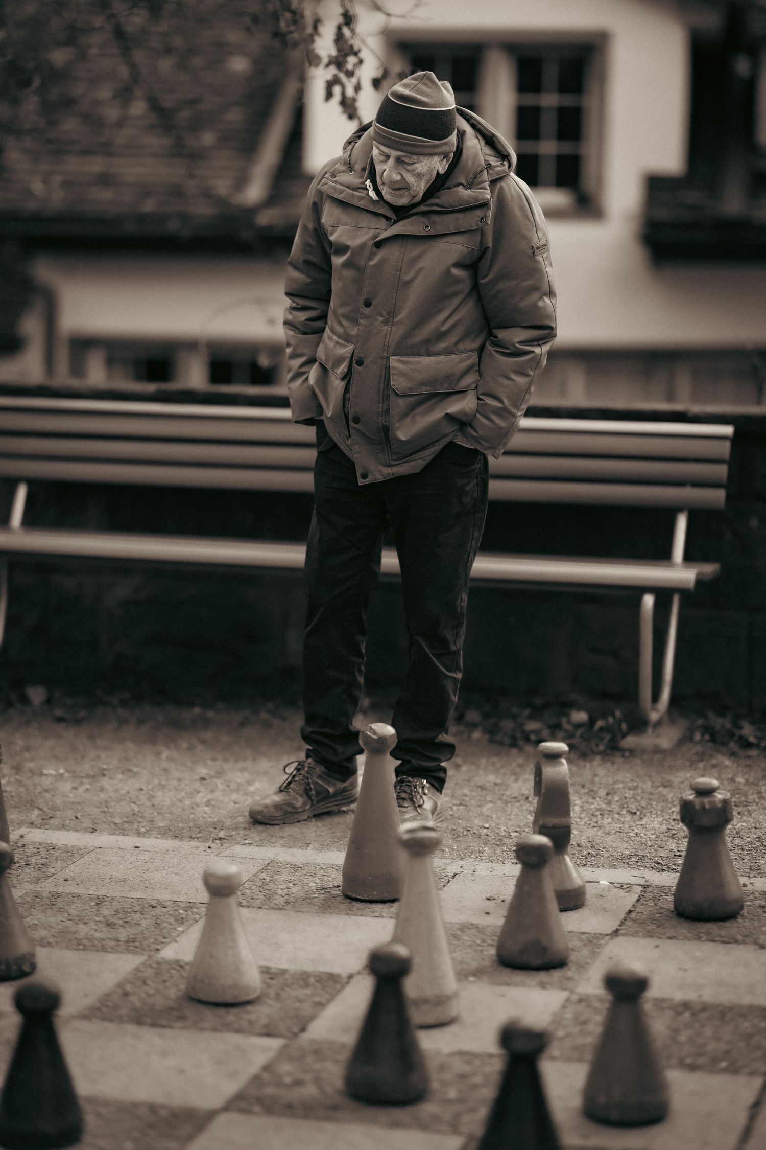 Giant chess pieces cast shadows on the ground as someone walks past in black and white.