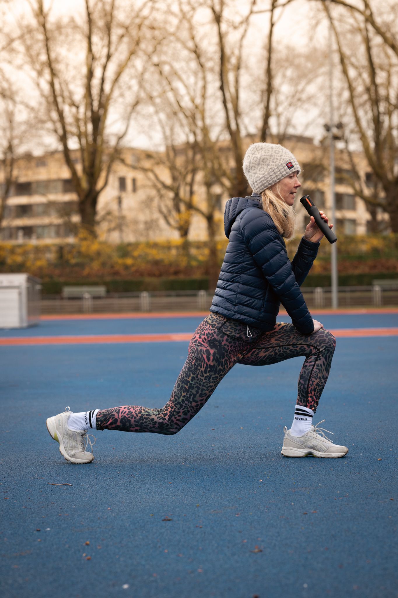 Person in winter workout gear performing lunges on a blue outdoor court surface.