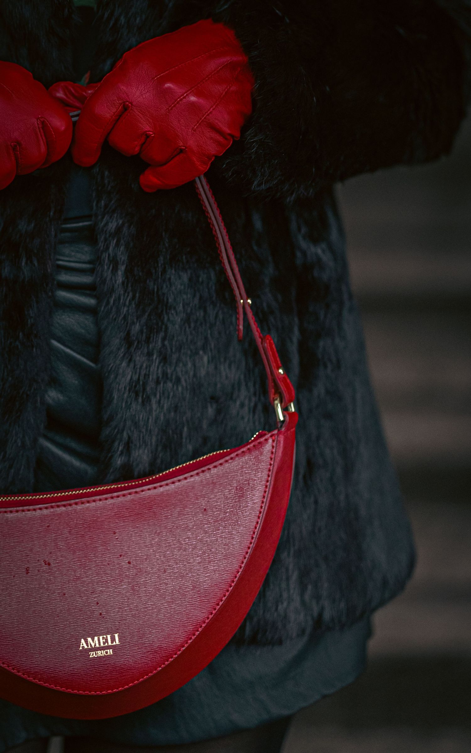 Red leather AMELI crescent shoulder bag held by a person wearing red gloves and a dark fur coat.