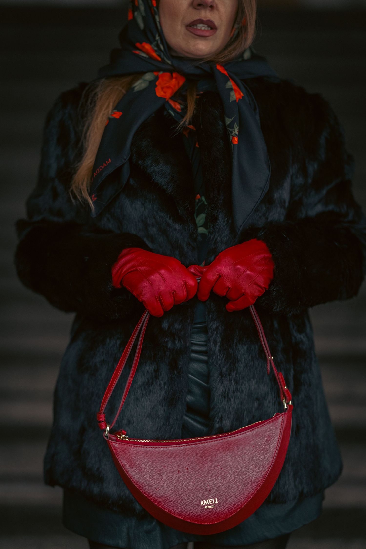 Woman in dark fur coat holding red leather Ameli handbag, wearing red gloves and floral scarf.