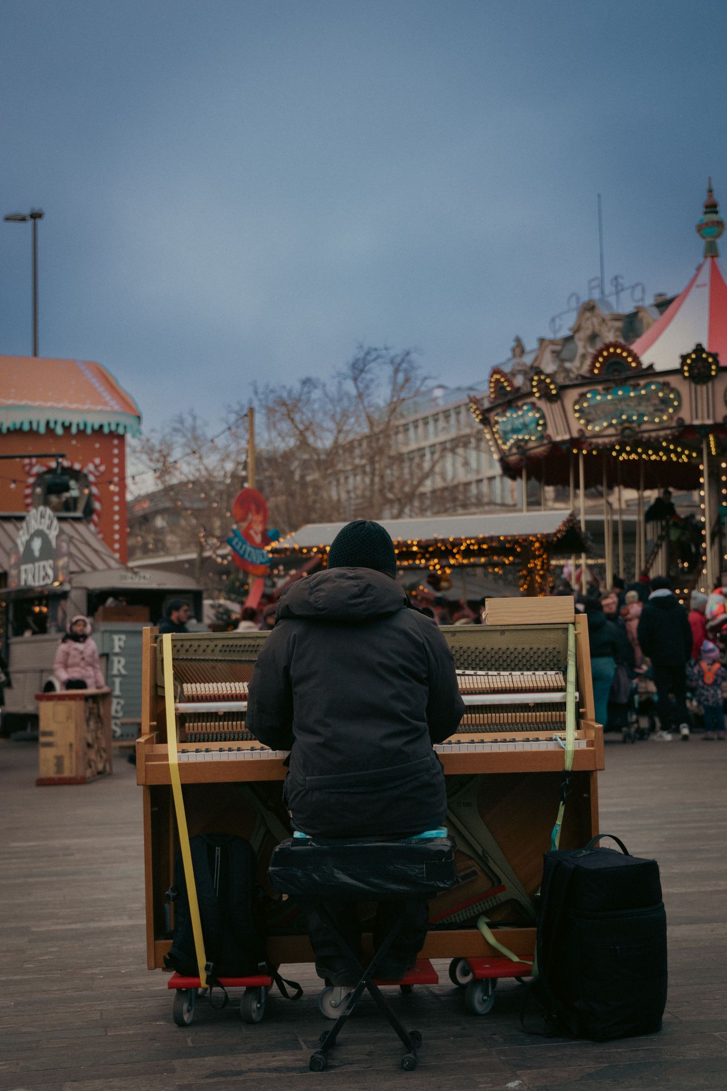 Public pianos arranged outdoors in city square with holiday decorations visible.