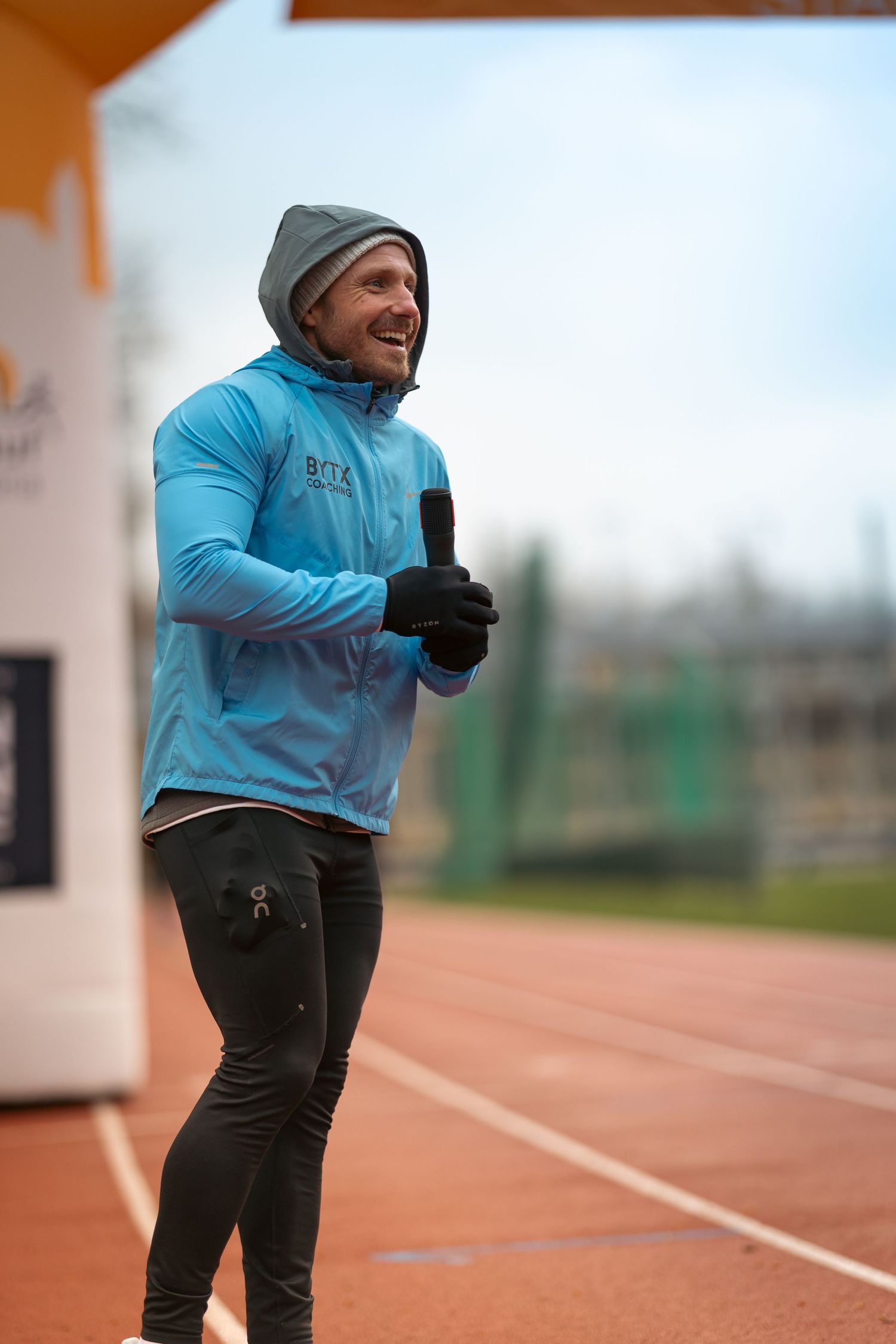 Athlete in light blue jacket running on outdoor track during training.