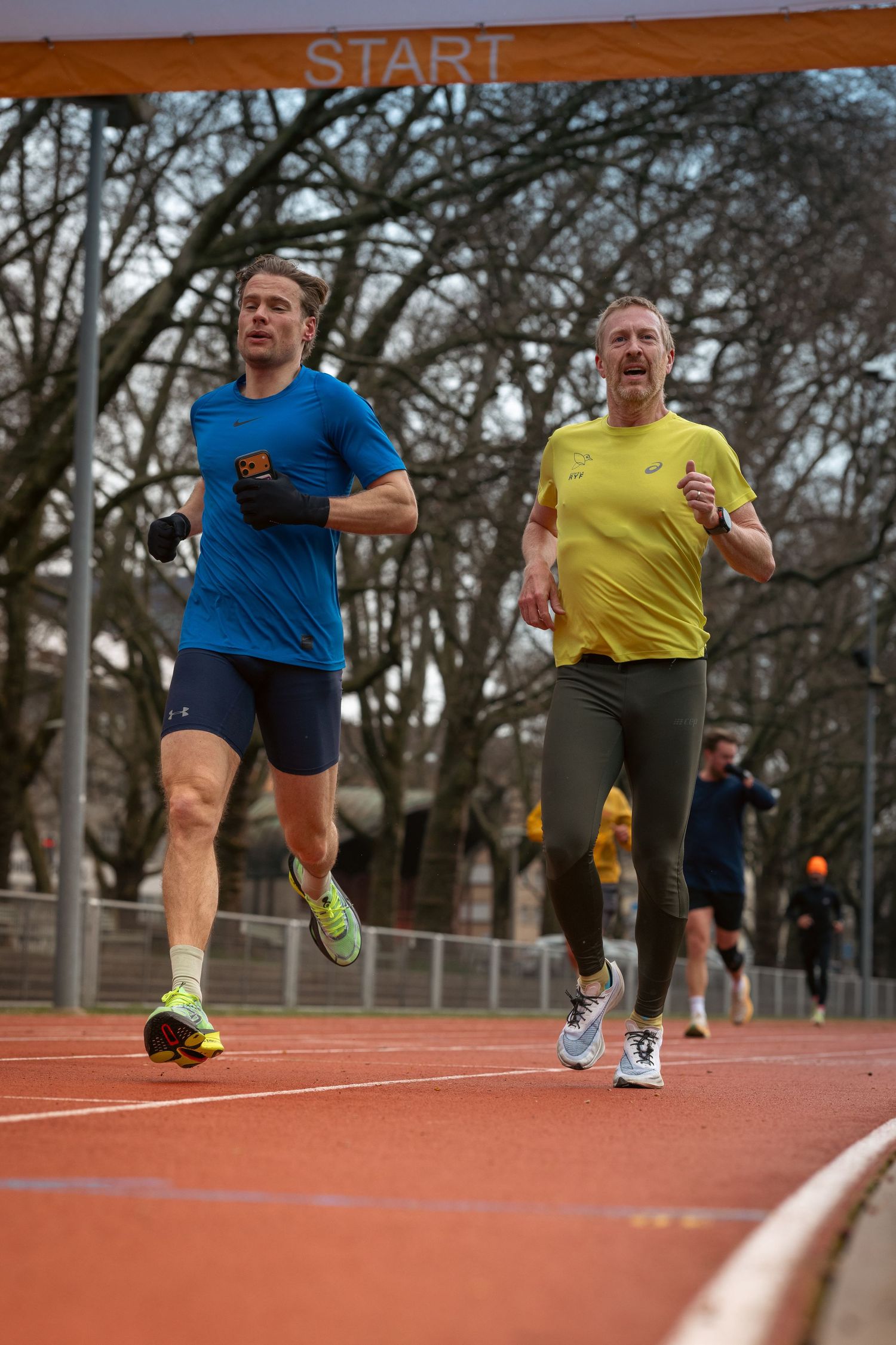 Group of athletes running on an outdoor track with START line visible.