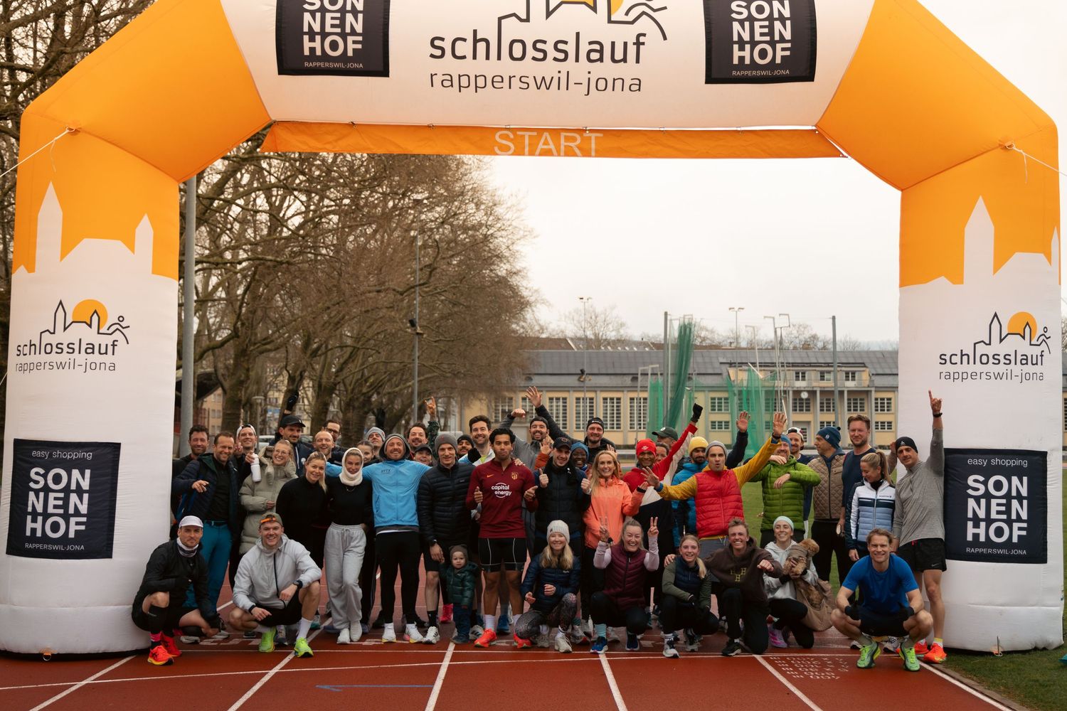 Large group photo of runners posing under orange finish arch at Schlosslauf running event.