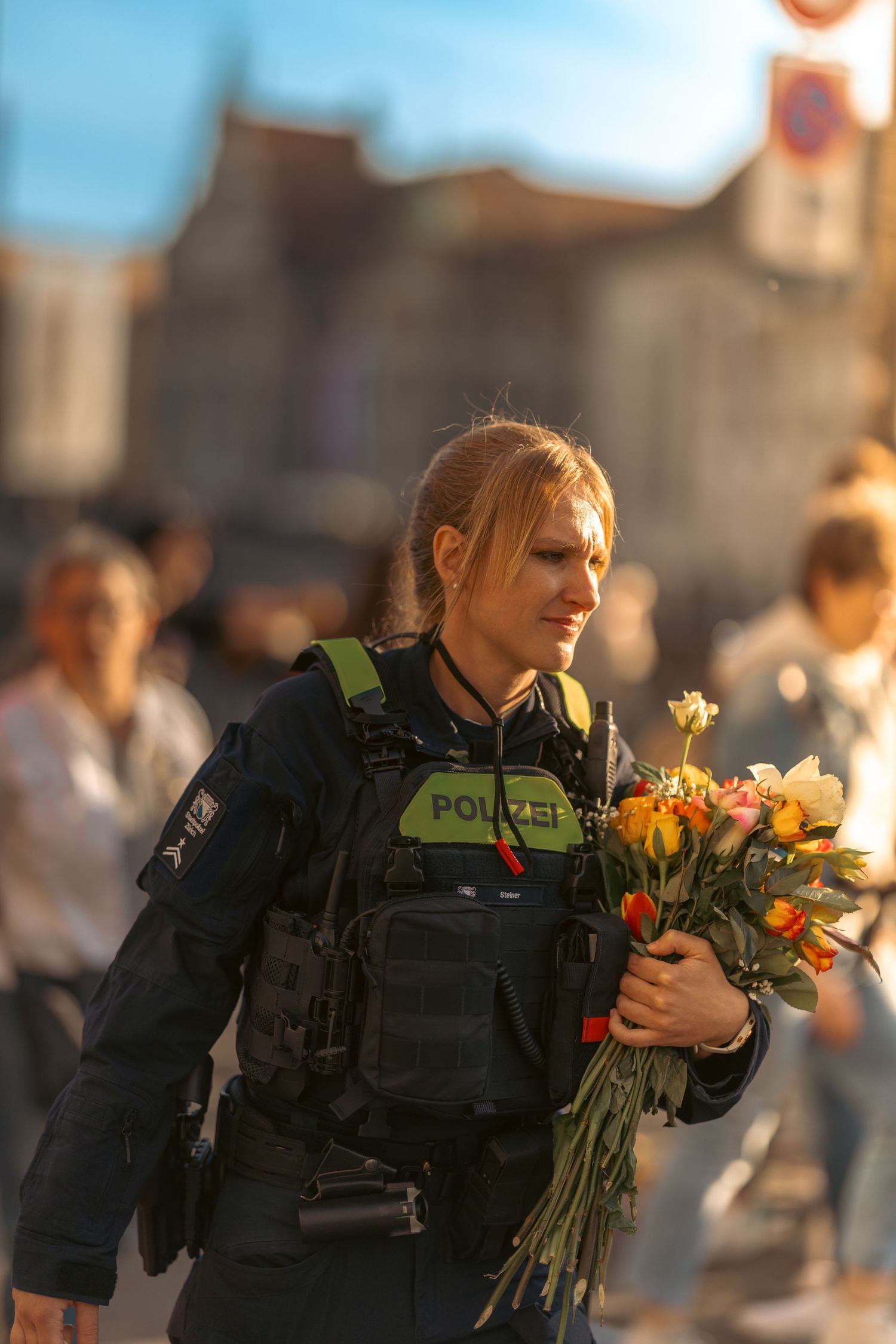 Female German Polizei officer holding colorful flower bouquet while on duty in a busy public square.
