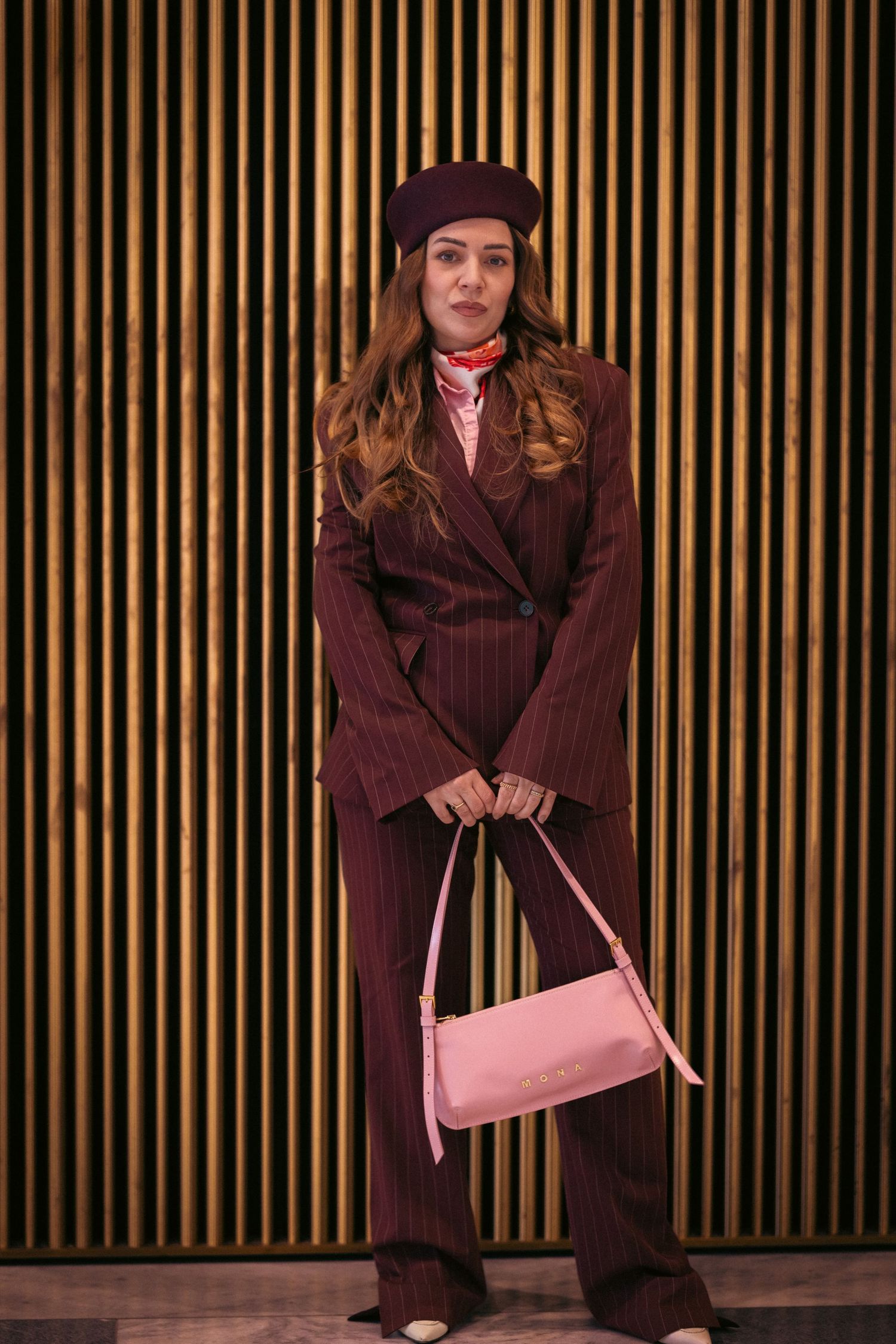 A series of four similar photos showing a person in a brown outfit posing against a striped background with a pink bag.