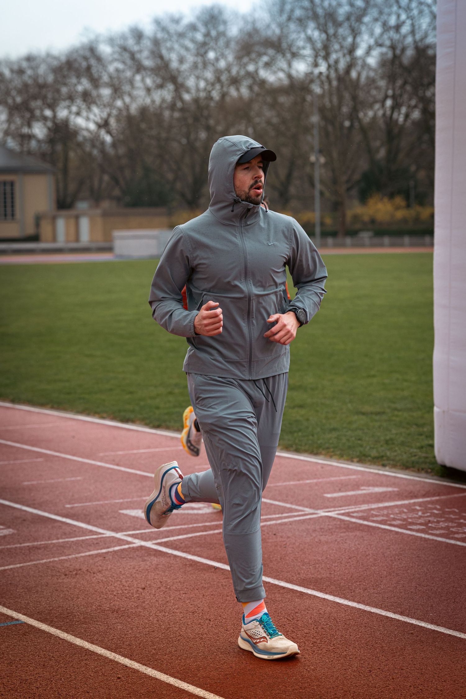Person in grey tracksuit jogging on a red running track during training.