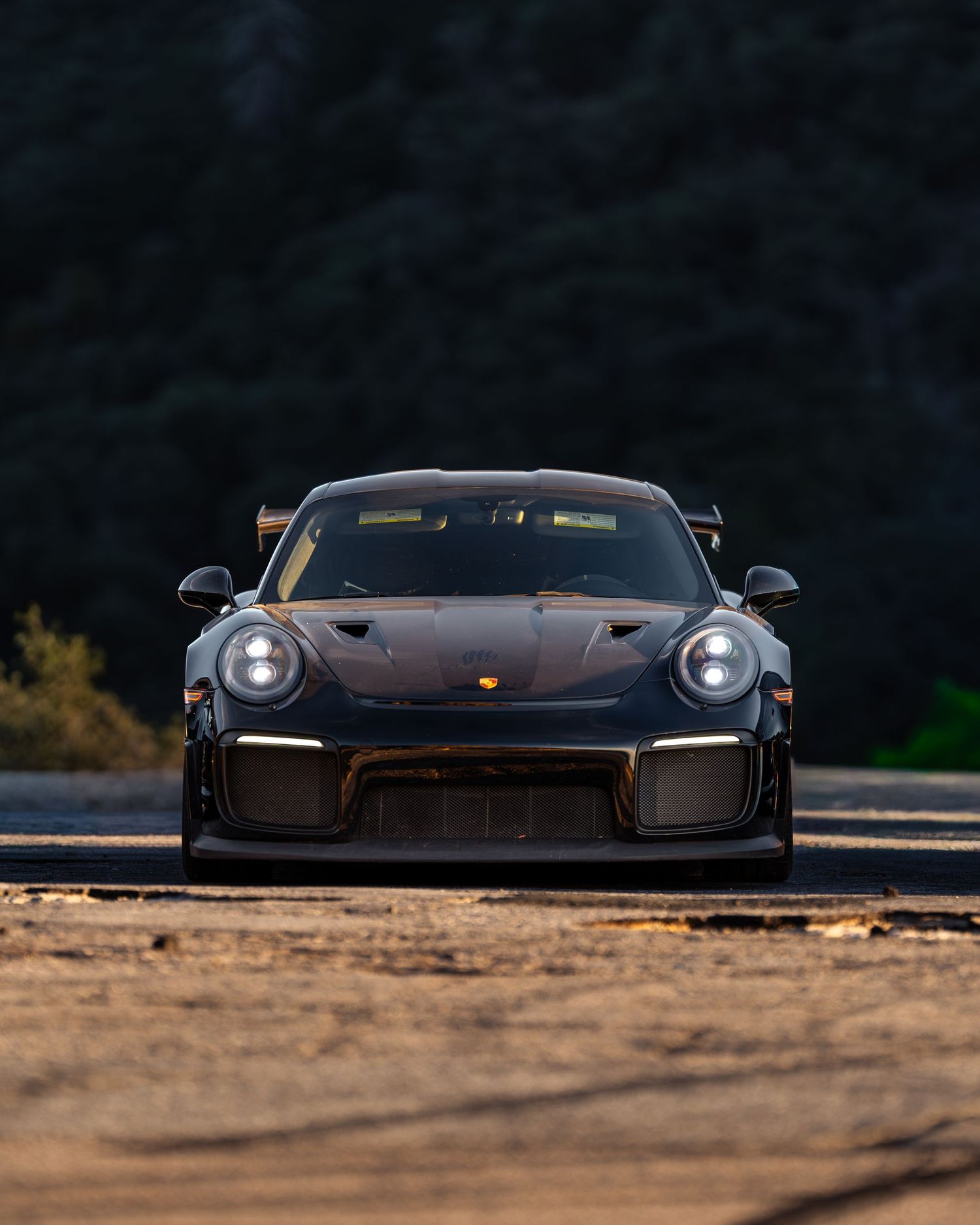 Dark Porsche sports cars lined up at sunset with dramatic lighting.