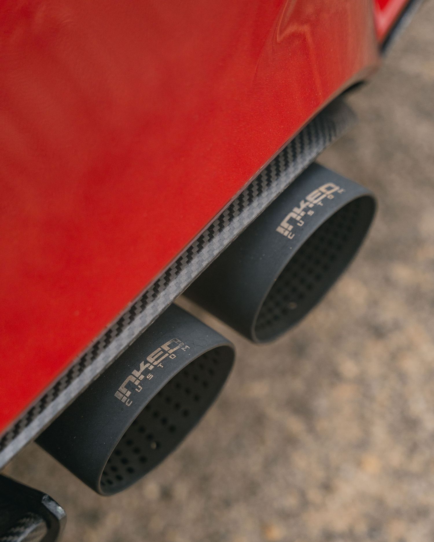 Close-up of dual black carbon fiber exhaust tips with INKED branding on a red sports car.