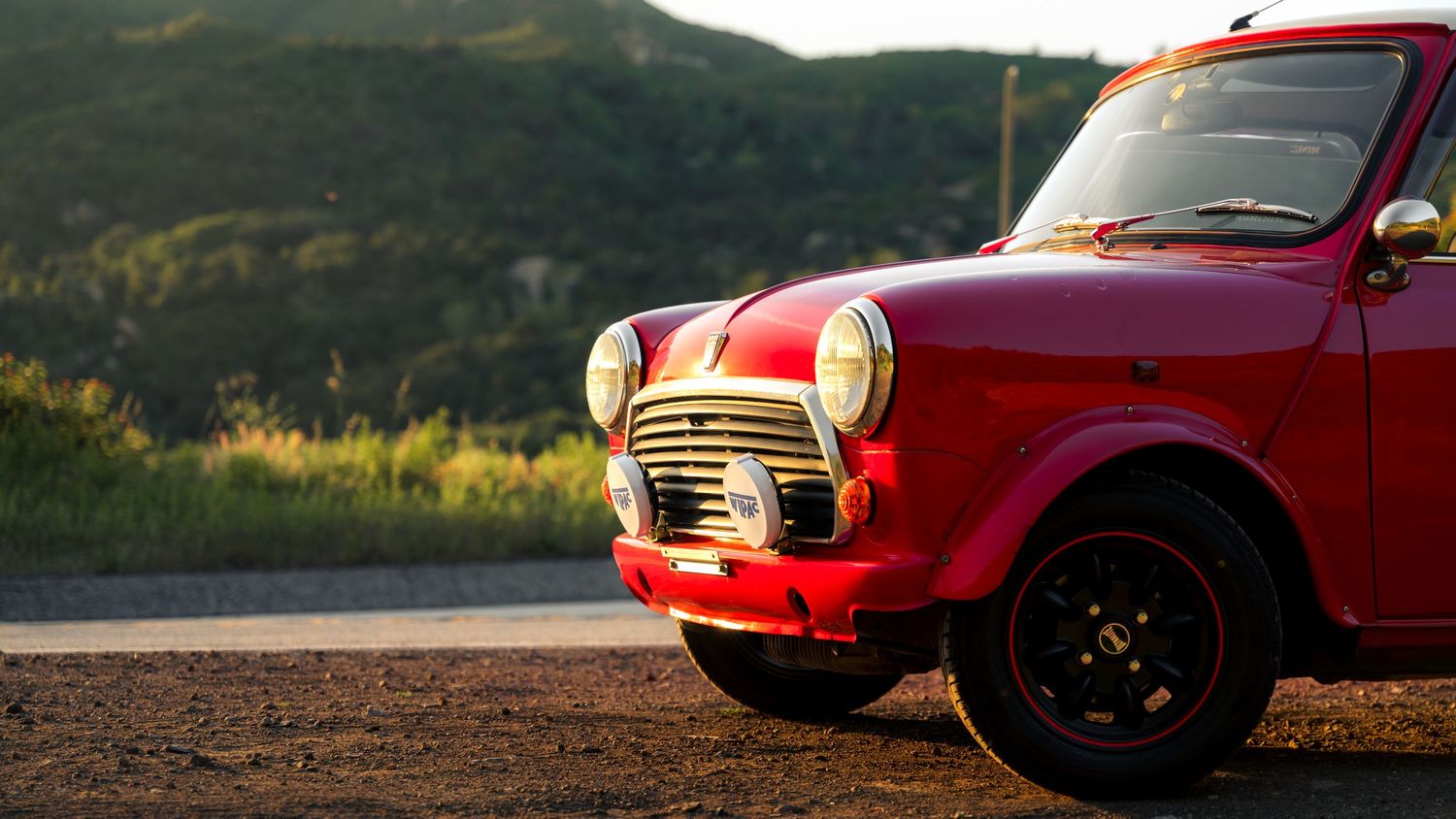 A series of red Mini Cooper cars lined up against scenic mountain and outdoor backgrounds in panoramic view.