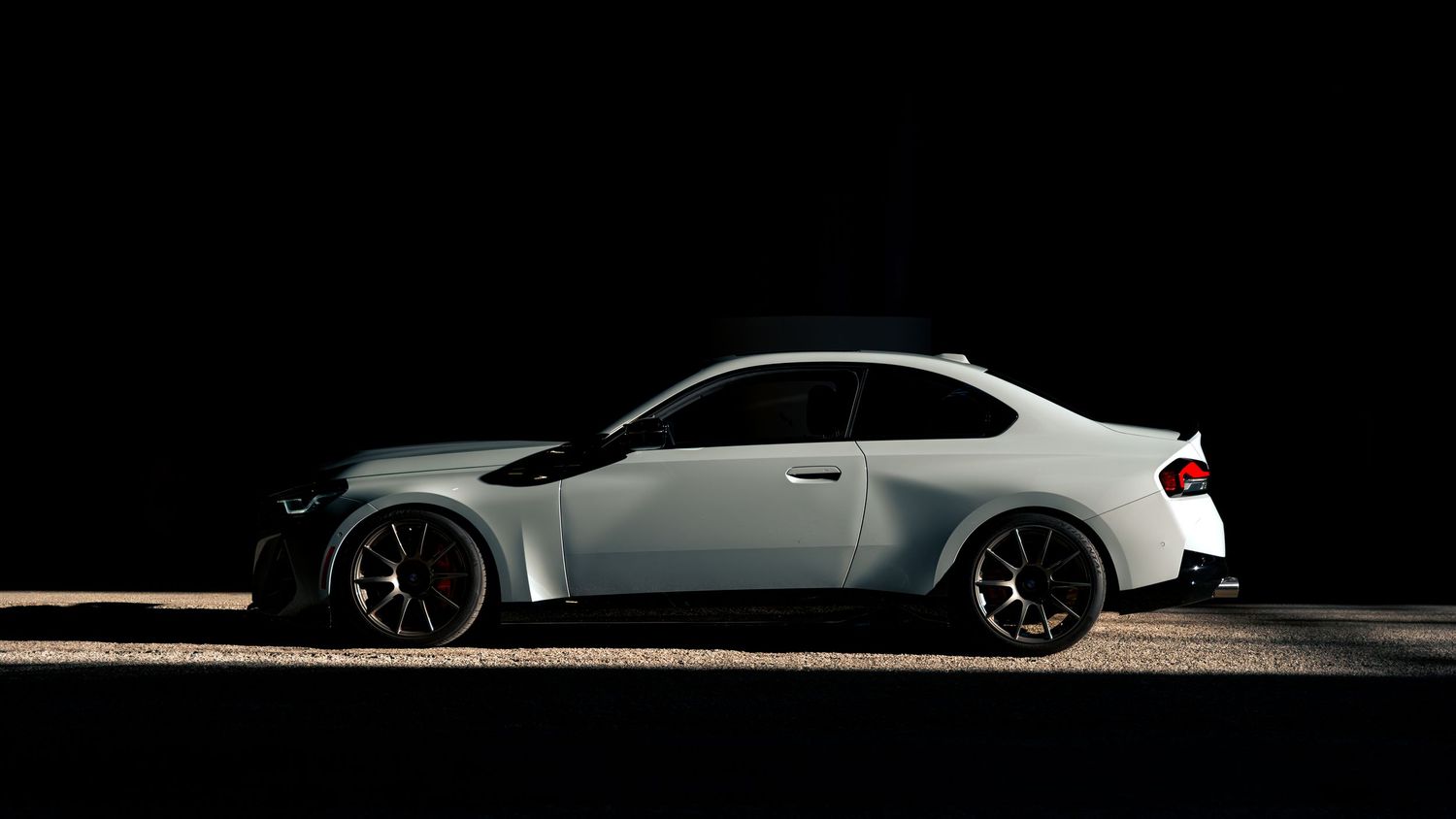 Dramatic low-light silhouette of a modified sports car with custom wheels against a dark background.