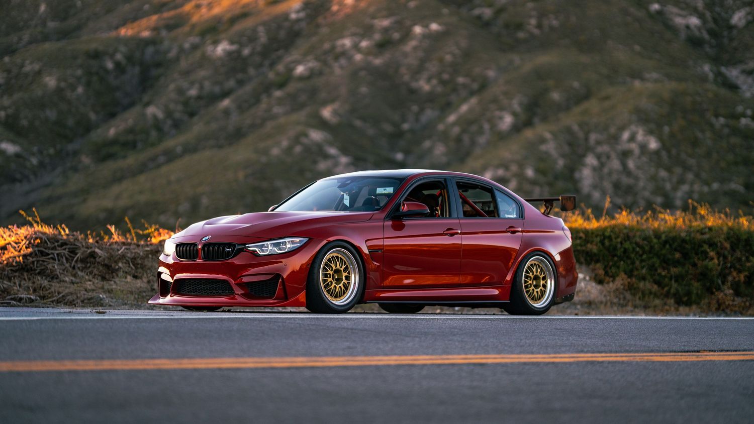 Luxury sports cars lined up against a mountainous backdrop during golden hour.