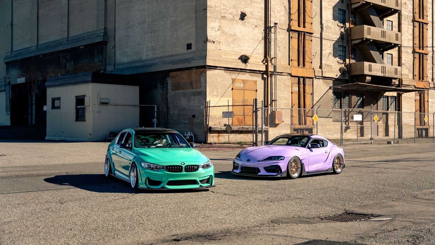 Row of colorful BMW vehicles parked in front of an industrial concrete building.