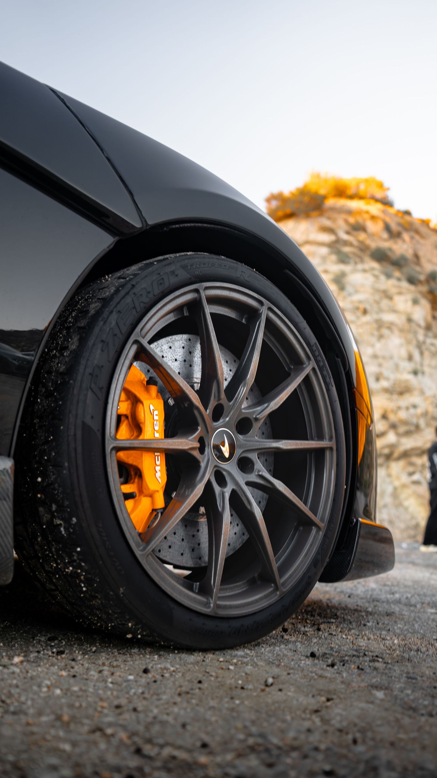Close-up shots of black sports car wheels with orange brake calipers against a rocky background.