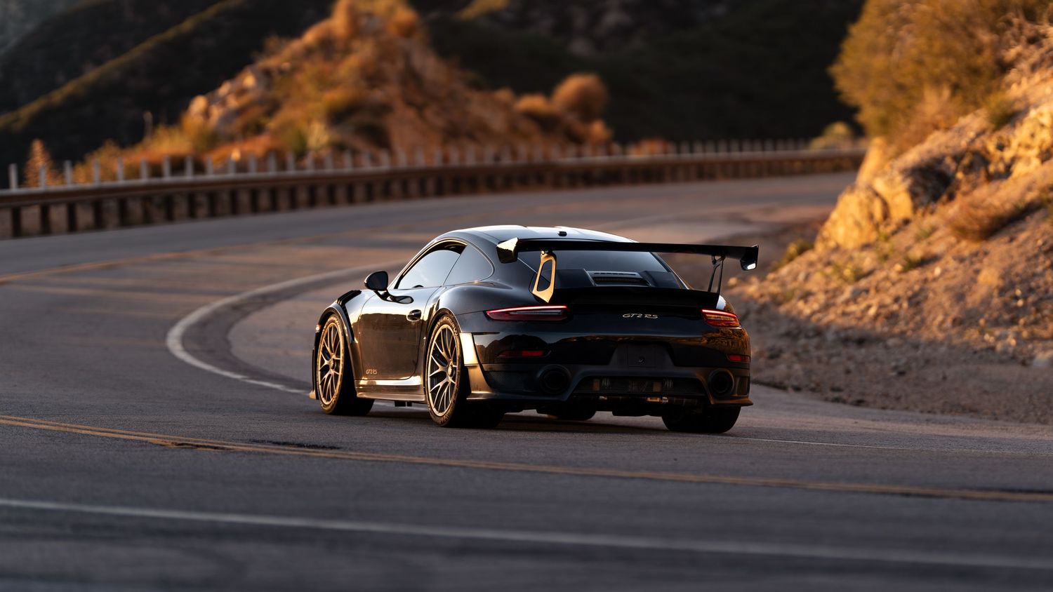 Low-angle view of sports cars on a mountain road during sunset.