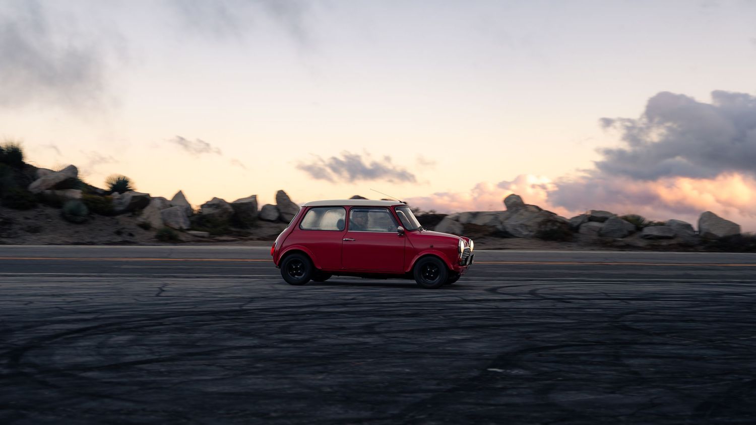 Panoramic view of a red classic car silhouetted against a dramatic mountain sunset.