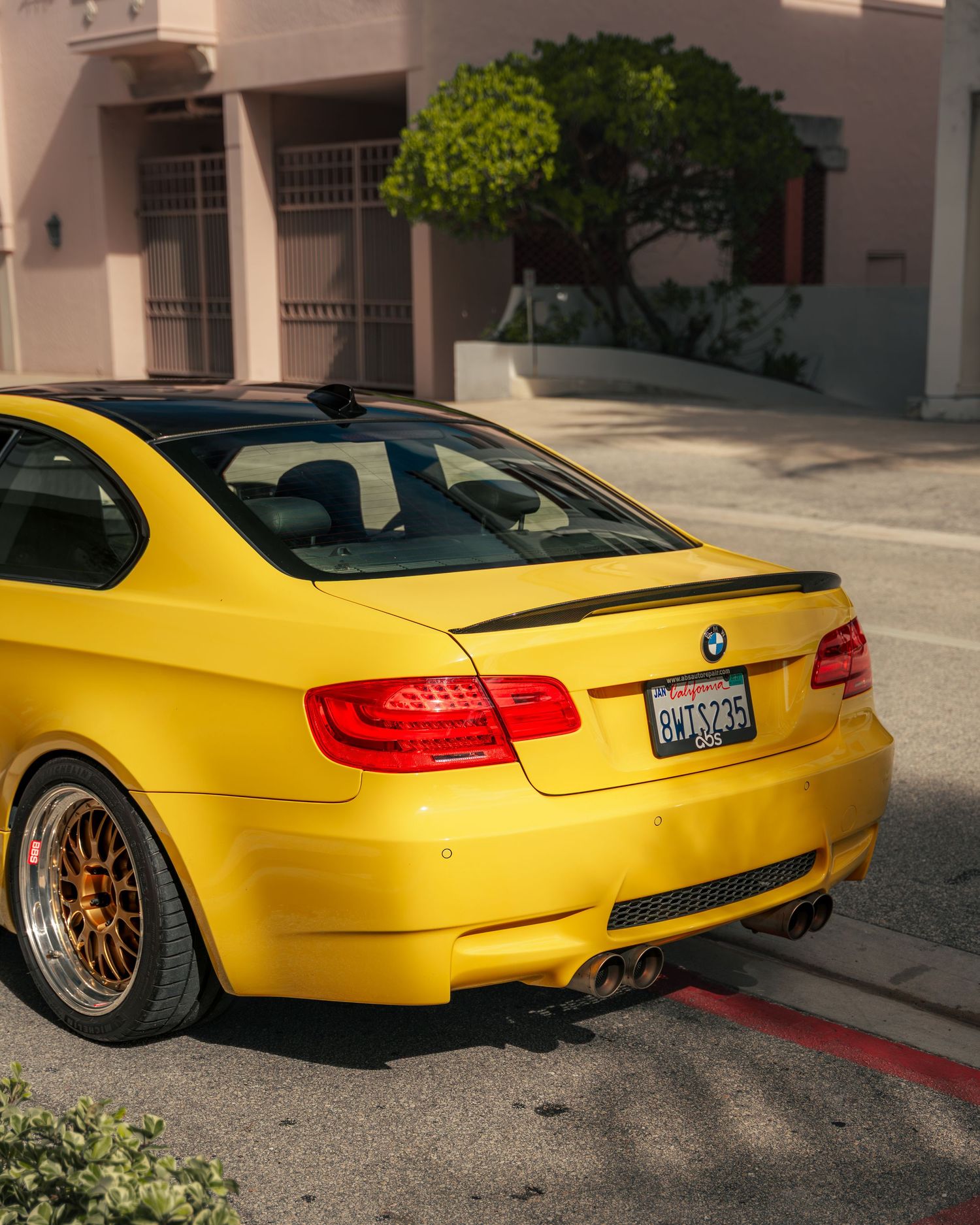 Bright yellow BMW M3 coupe with gold wheels and black spoiler parked on a street in California.
