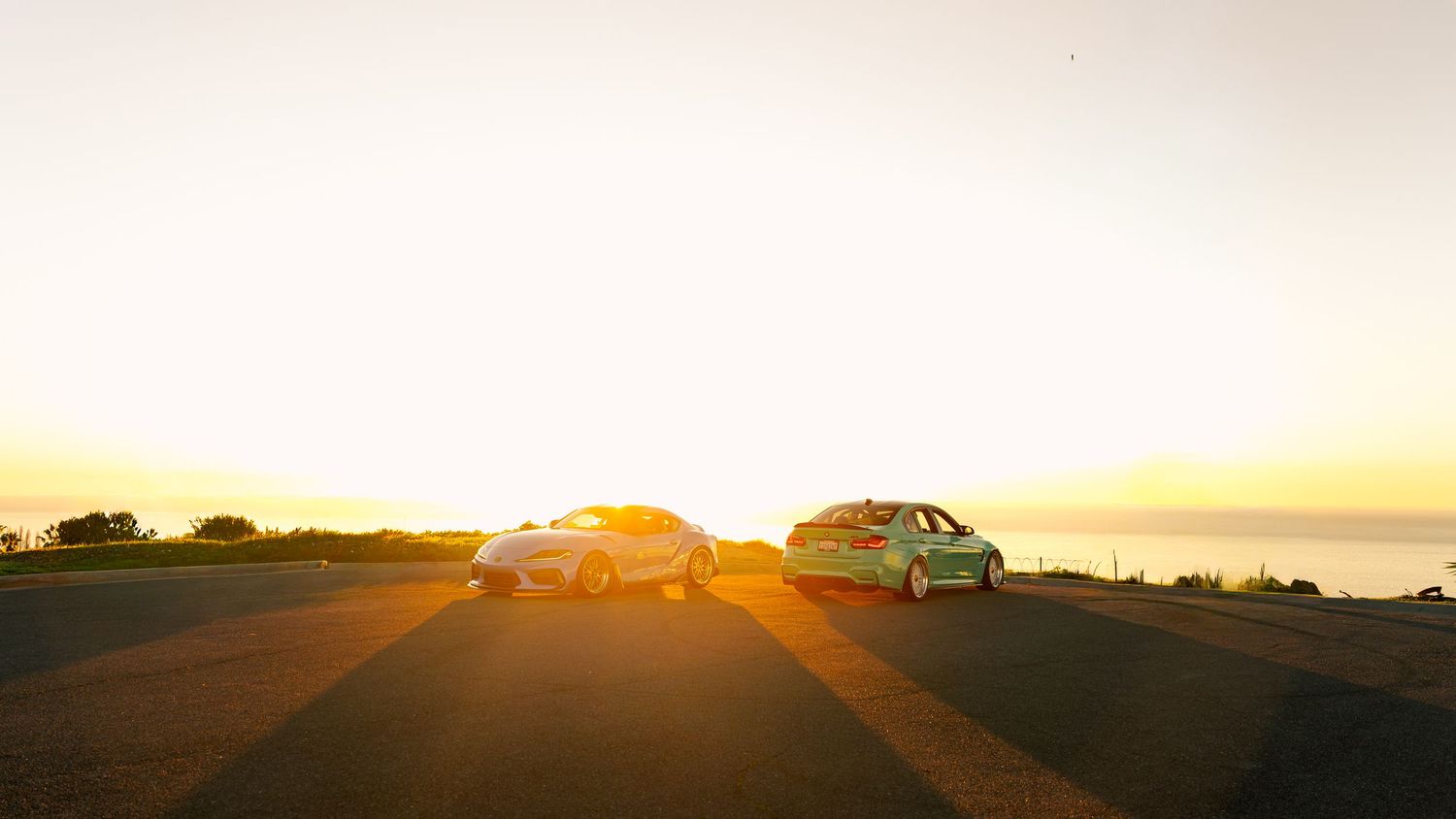 Collection of exotic cars displayed on coastal road at dusk.