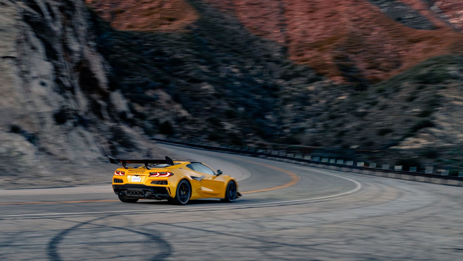 Colorful sports cars navigating curved mountain road against rocky terrain.
