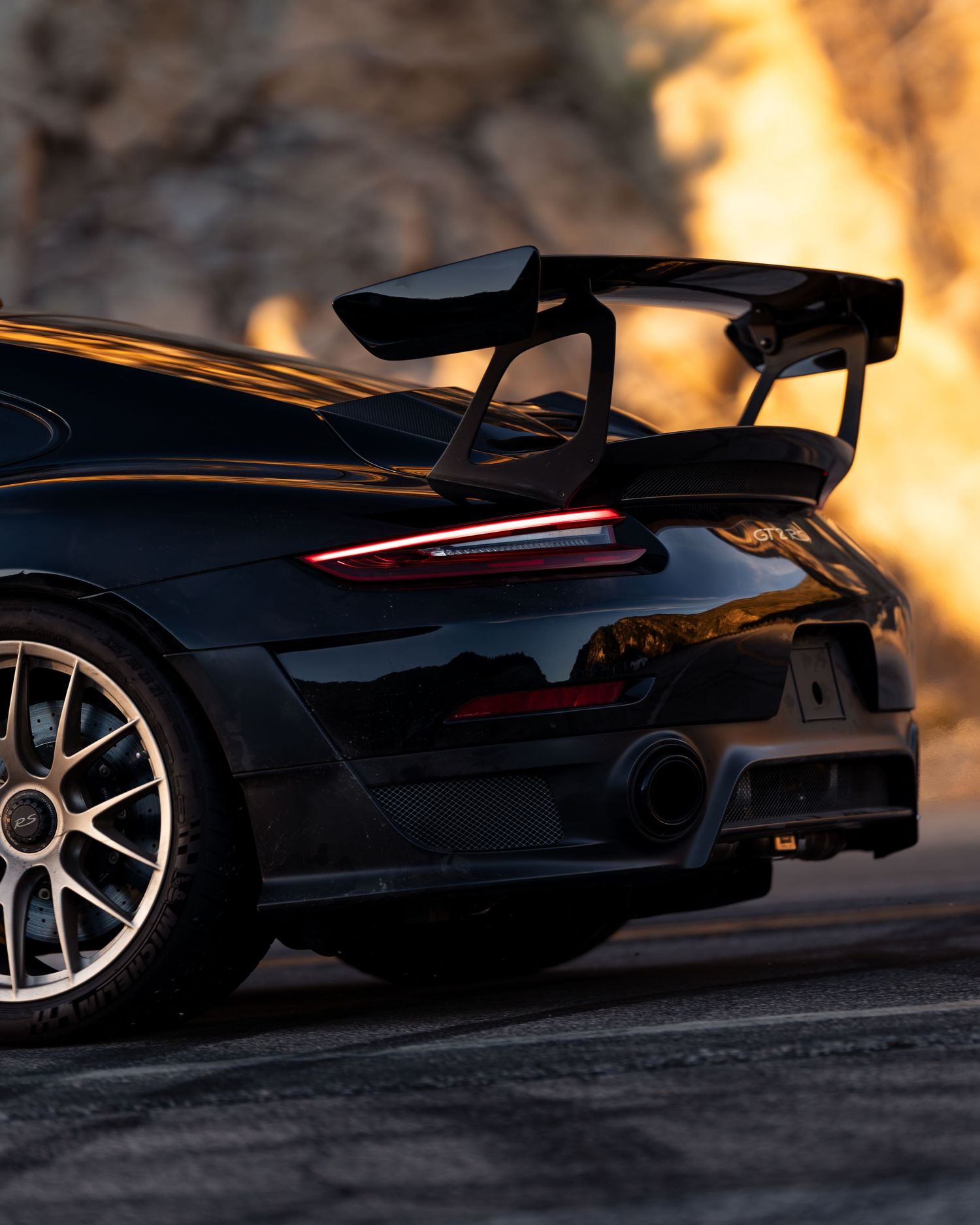 Silhouette of sports car with large rear wing against warm sunset lighting.