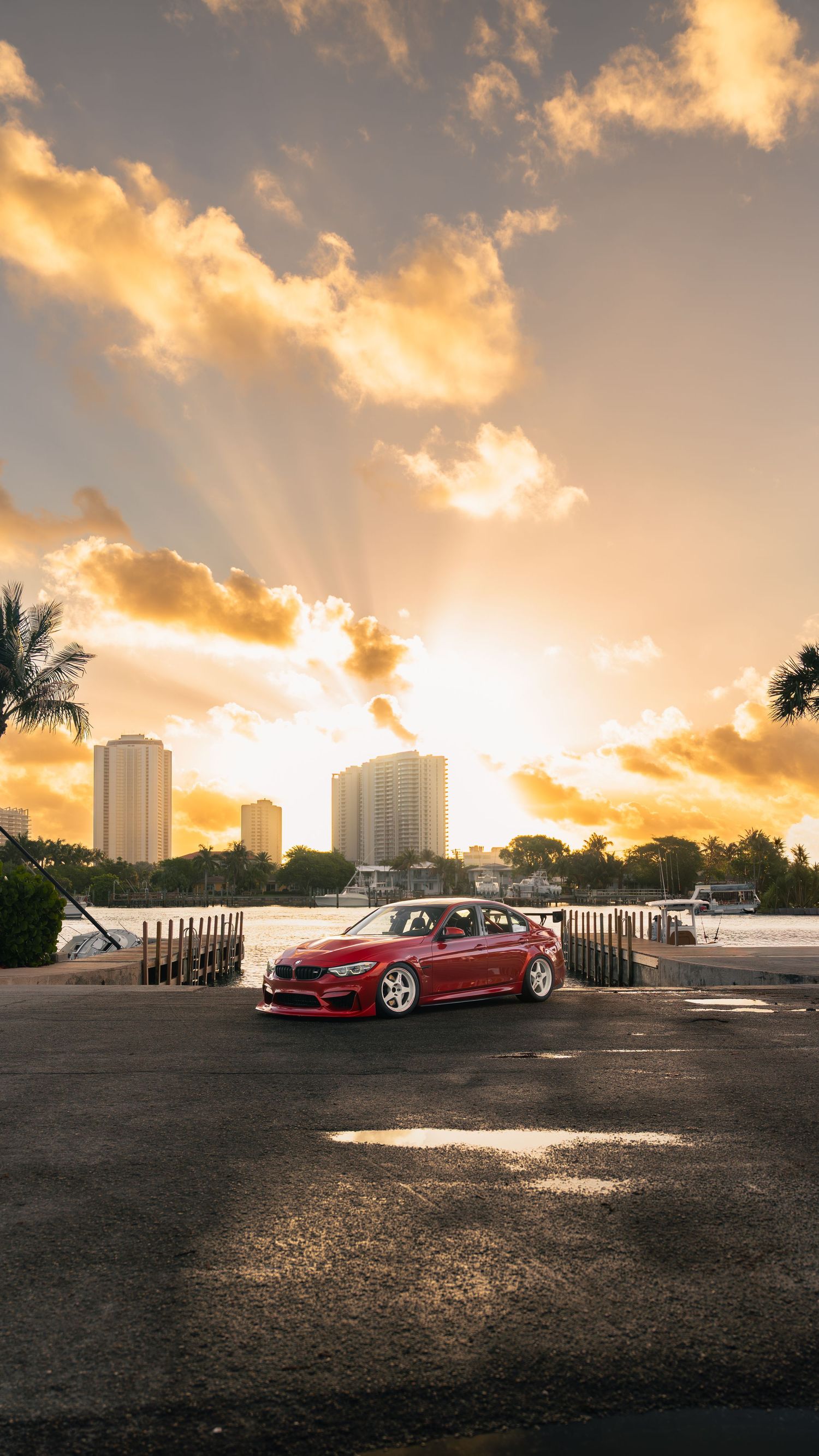 Red BMW sports car parked at sunset with dramatic golden sky, city skyline, and palm trees in the background.