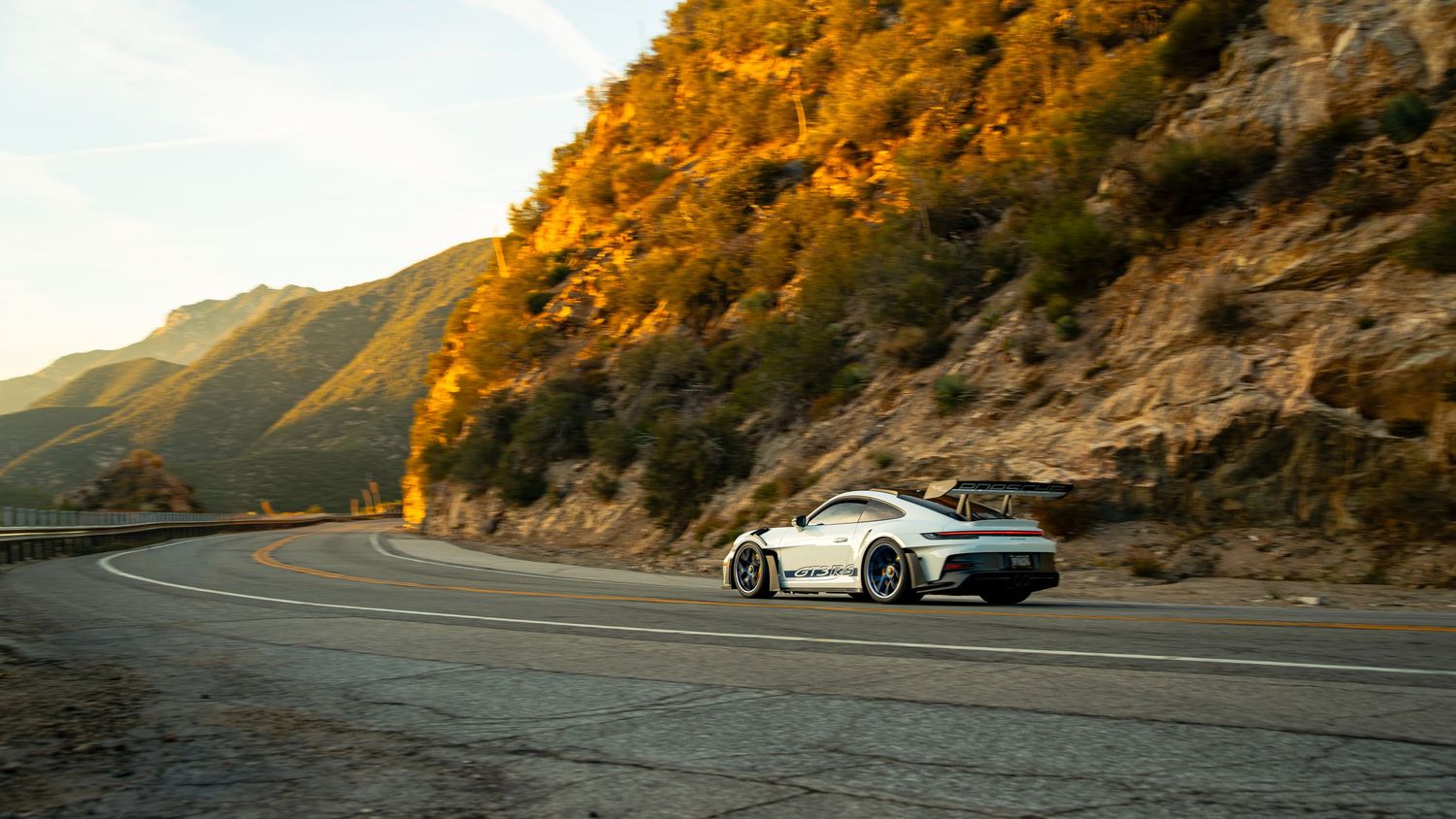 White sports car navigating curved mountain road during golden hour.