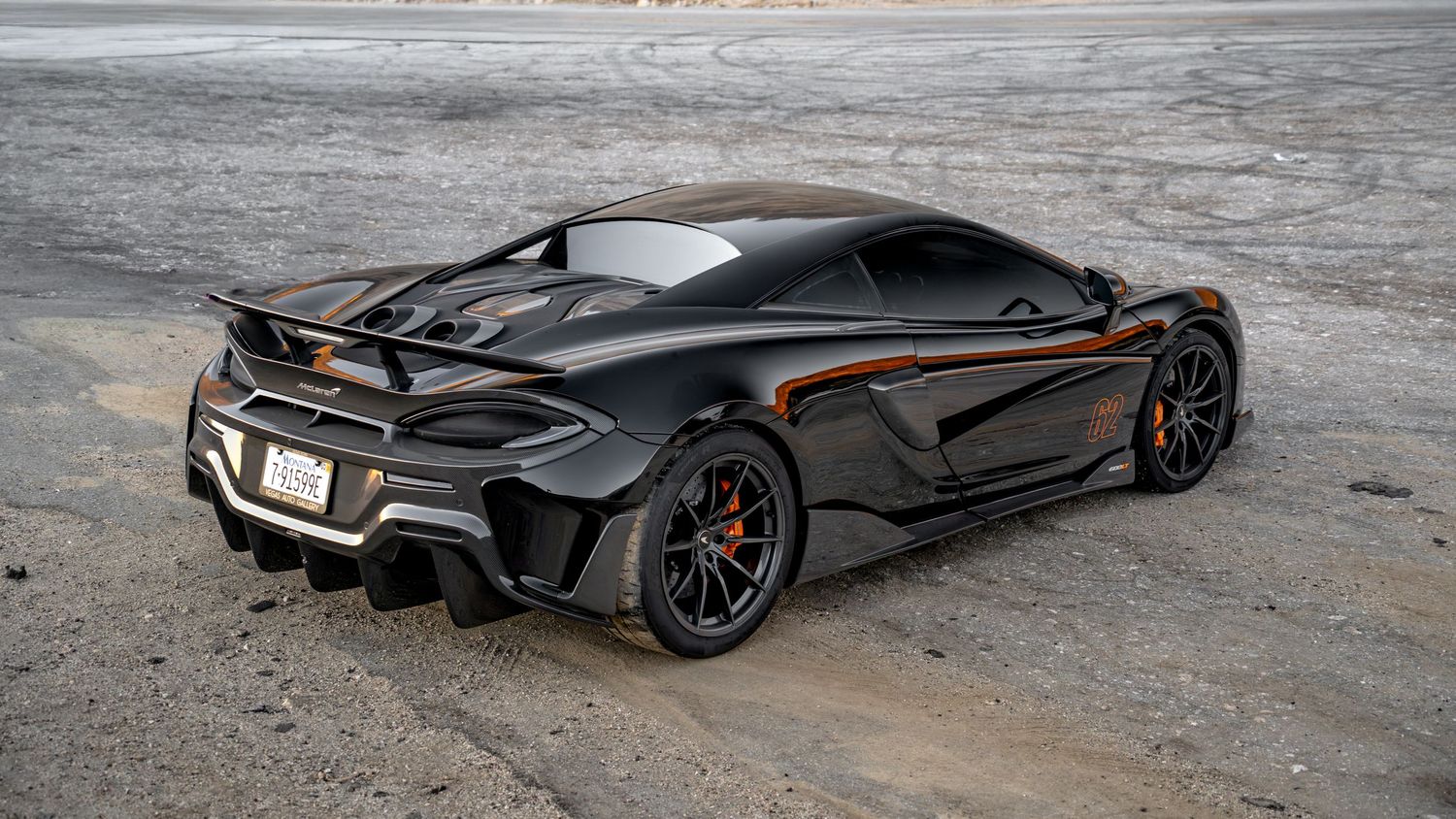Wide panoramic shot of a sleek black sports car against an industrial backdrop.
