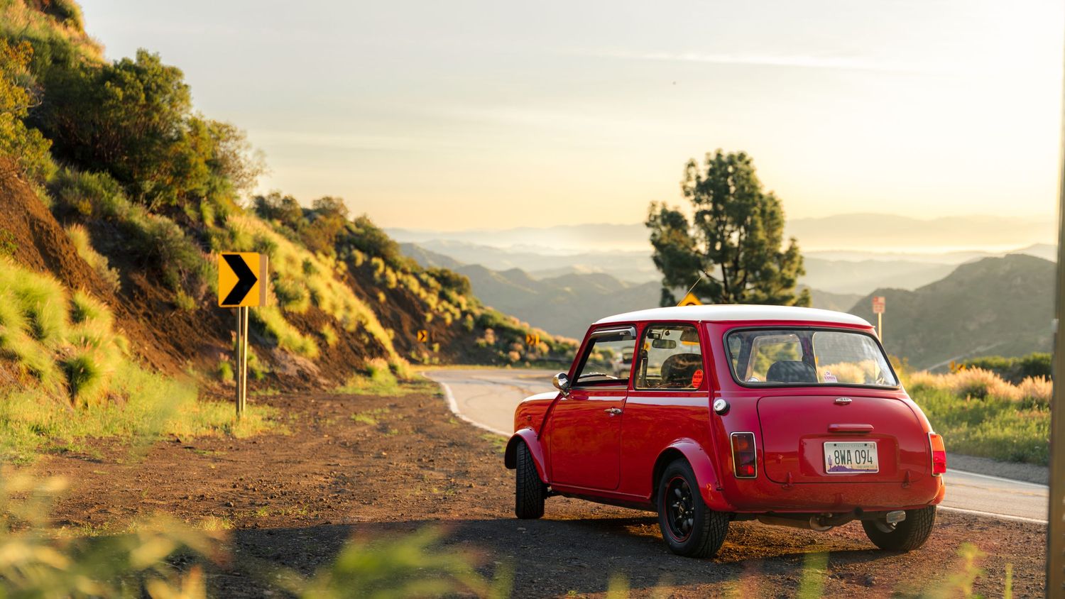 Classic red vintage cars parked along scenic mountain roads at sunset, creating a nostalgic automotive scene.