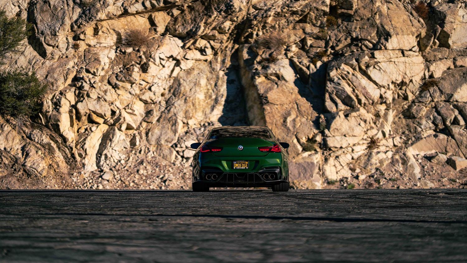 Rocky cliff face backdrop with luxury vehicles silhouetted against the terrain.