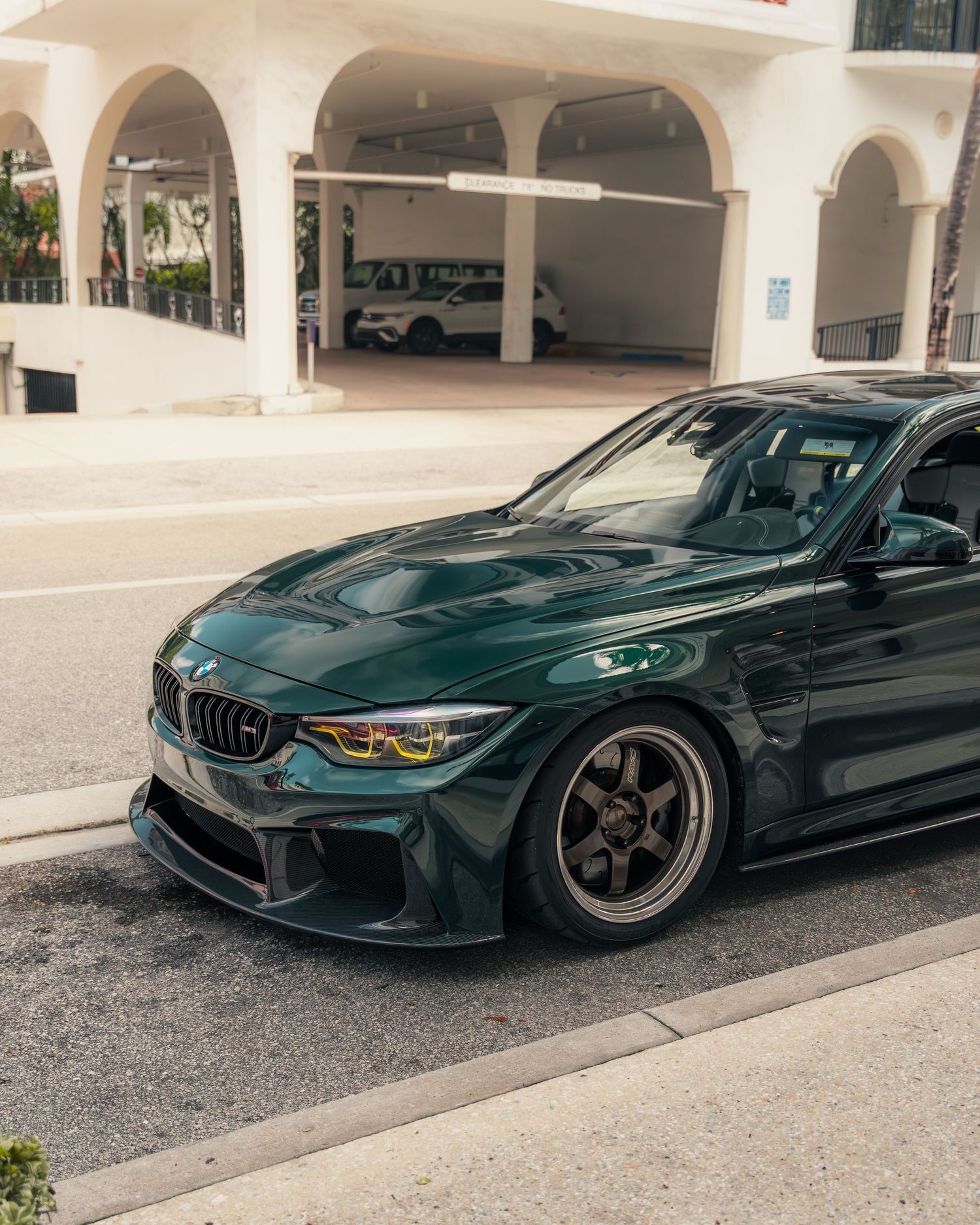 Dark green BMW M3 with wide body kit and bronze wheels parked outside a white building.