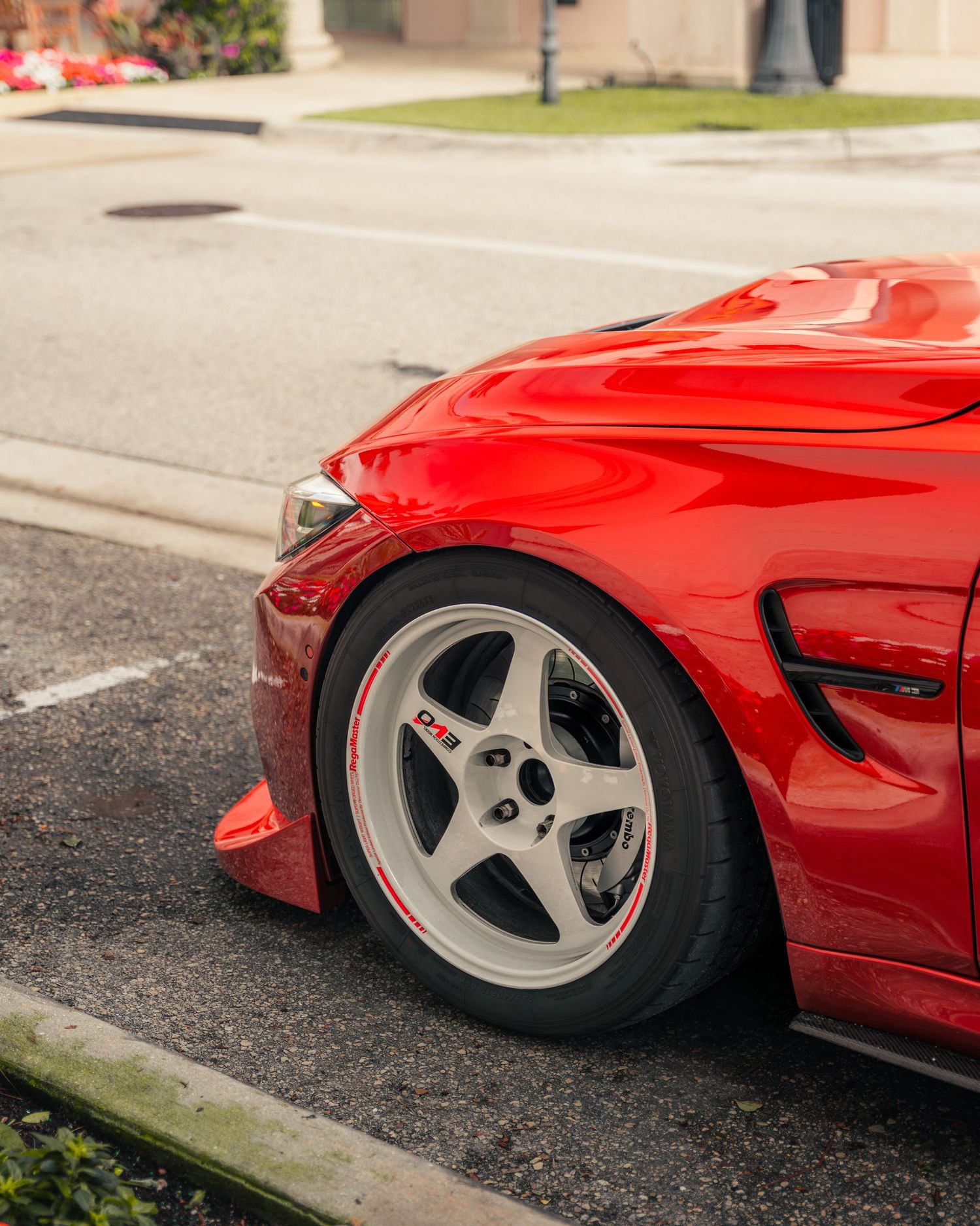 Red sports car with white five-spoke wheels parked on a street, showcasing a lowered stance and aggressive body kit.
