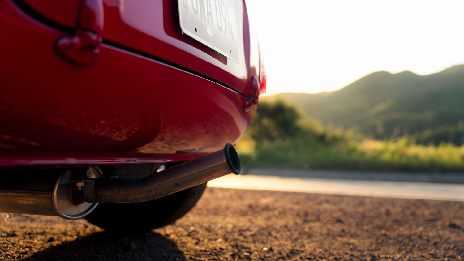 Red sports car driving on winding mountain road at sunset with dramatic lighting and shadows.