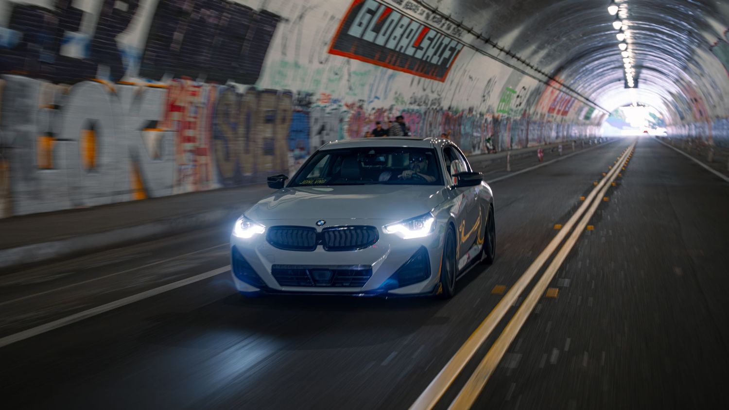 BMW sports car driving through an illuminated tunnel with graffiti-covered walls.