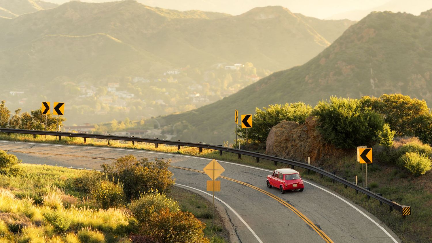 A scenic winding mountain road curves through golden hills at sunset with a red car driving along the highway.