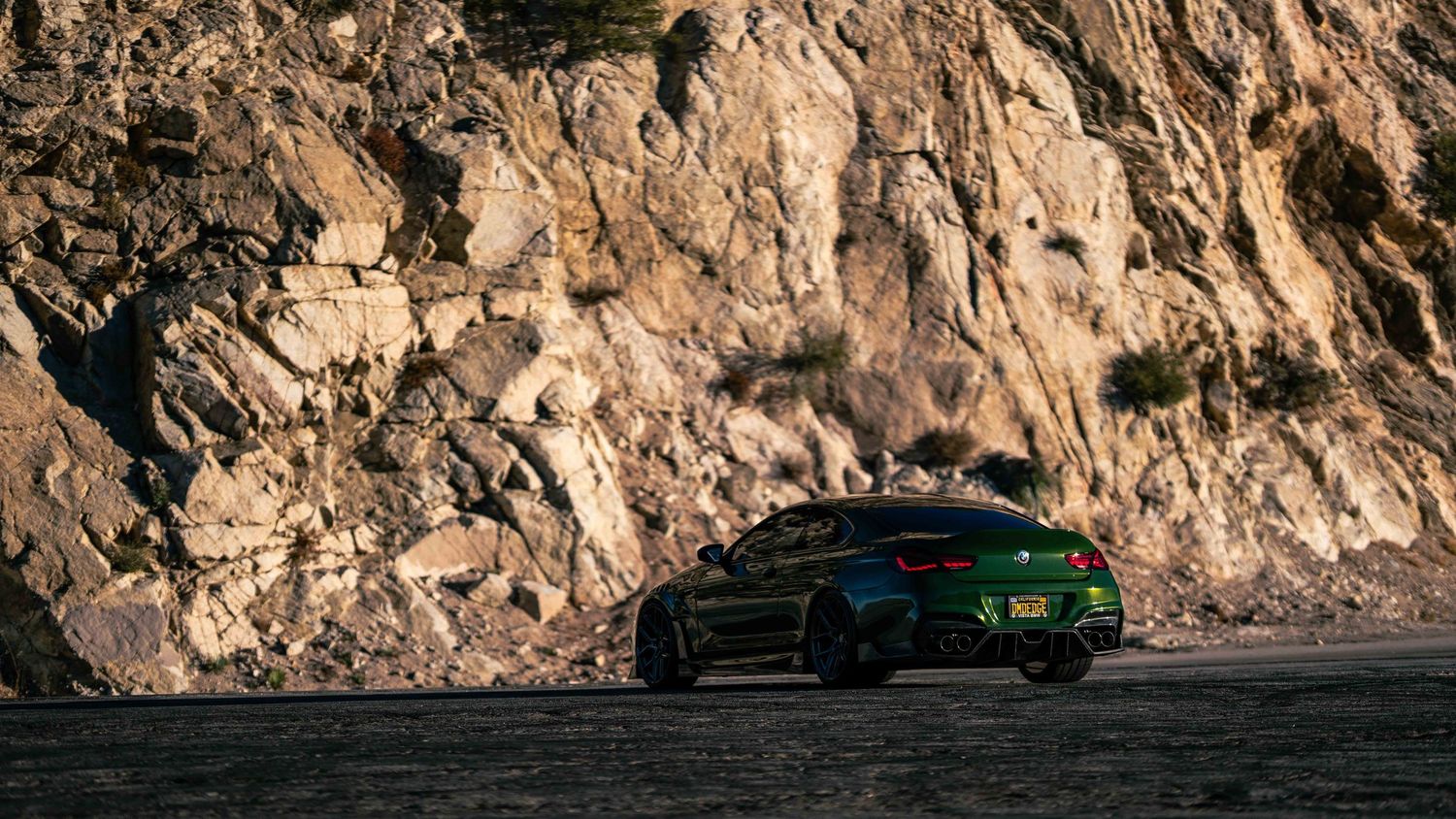 Green sports car parked near rocky mountain terrain during sunset.