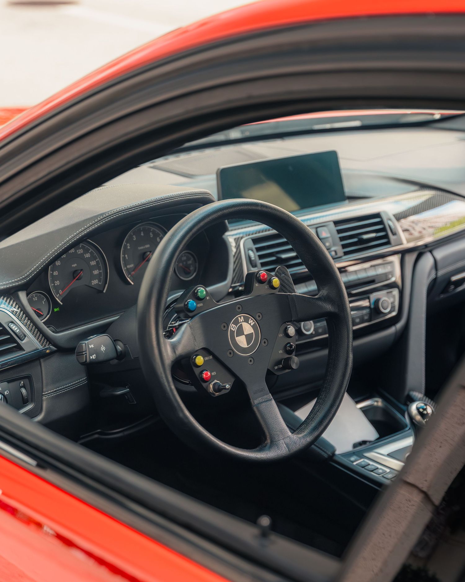 Interior view of a red BMW with a racing steering wheel featuring colorful buttons and a digital display dashboard.