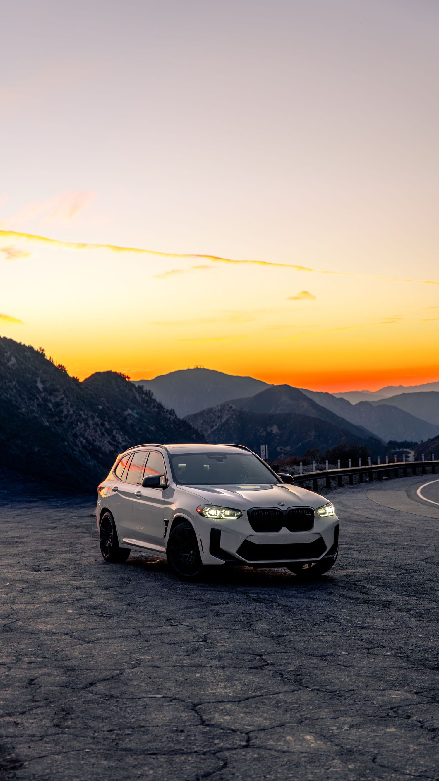 White BMW M cars lined up at dusk with mountains silhouetted in the background.