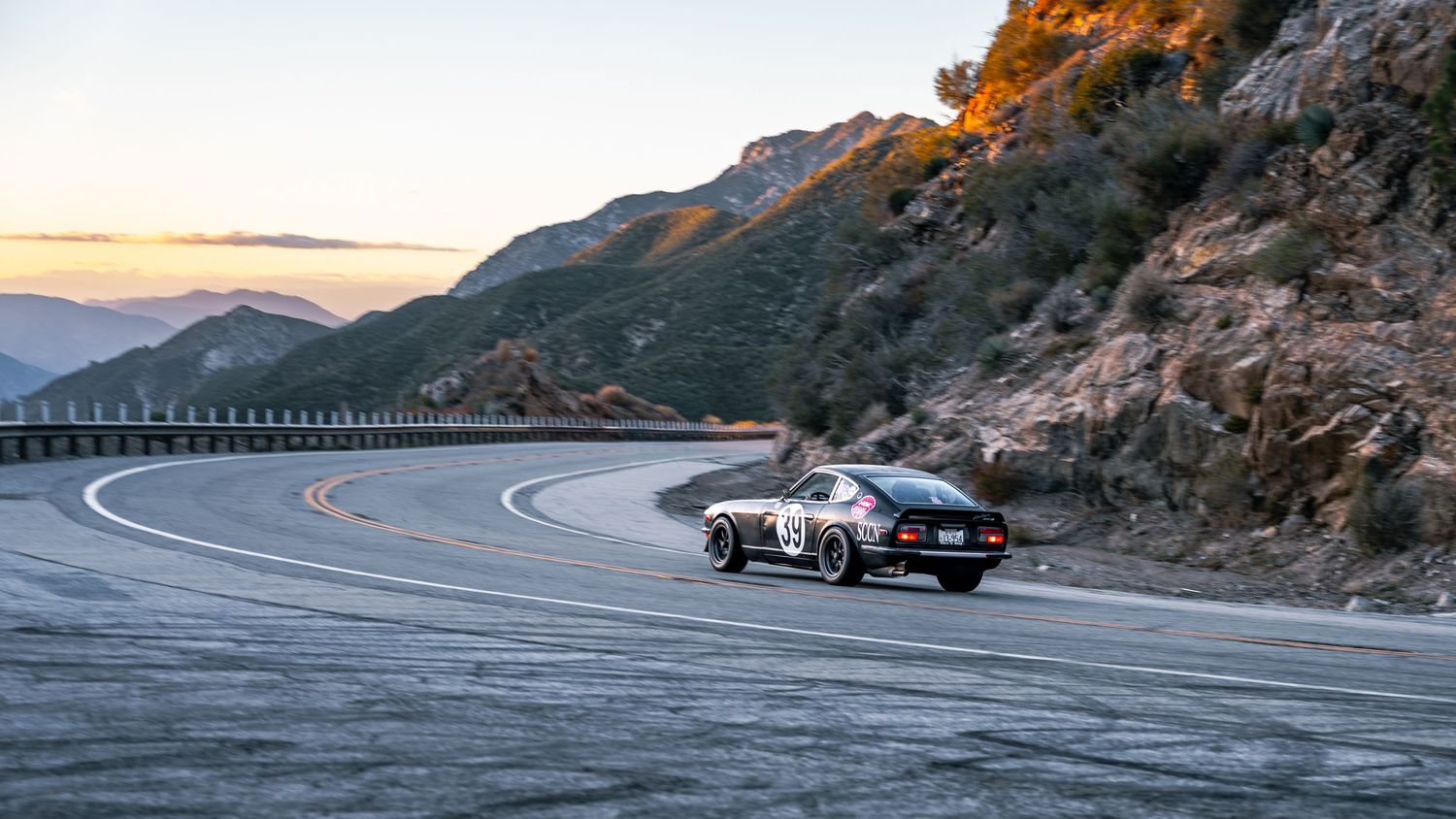 Classic cars navigating scenic mountain roads during golden hour.