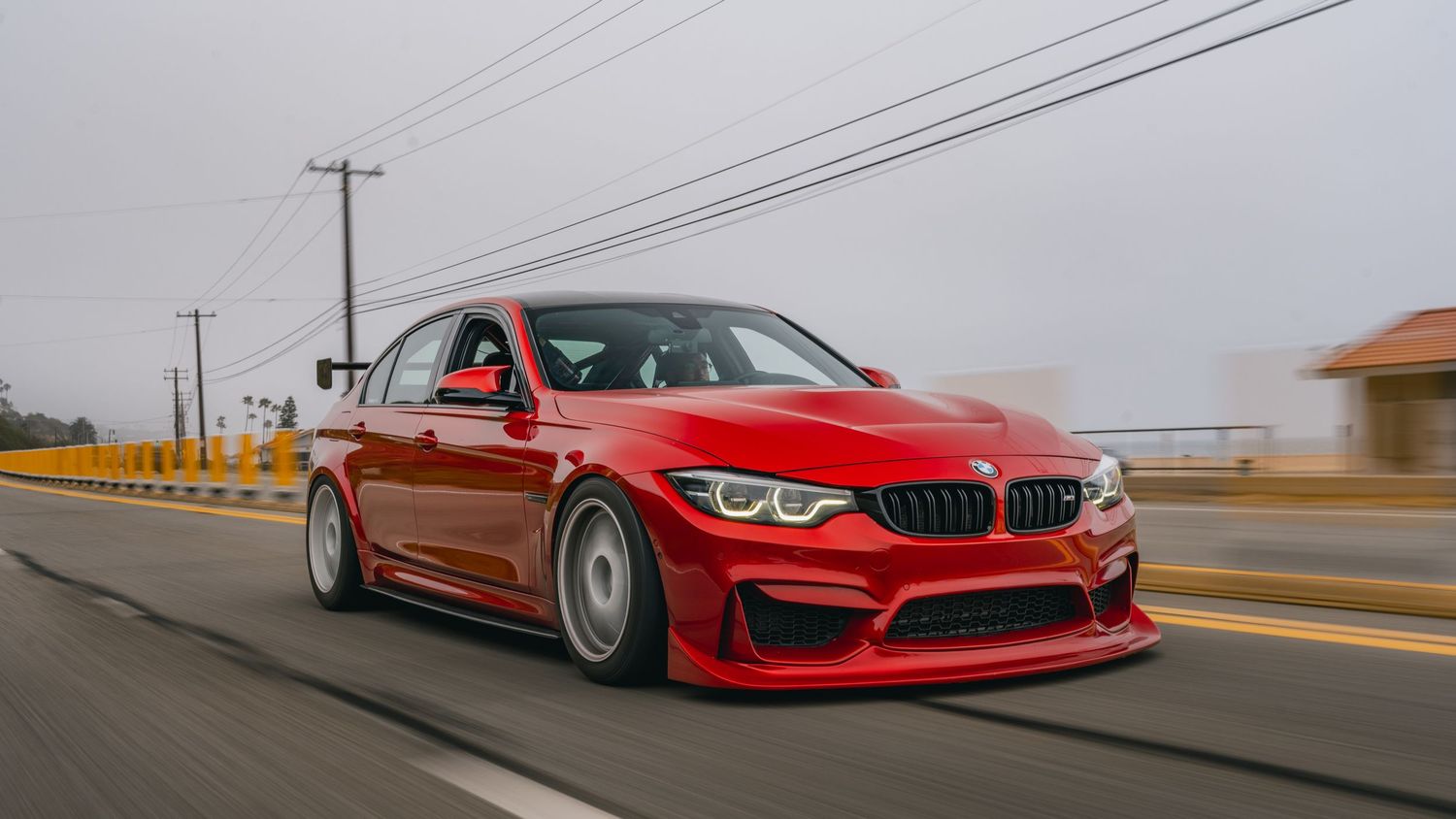 Red BMW M3 with wide body kit driving fast on a road with motion blur background.