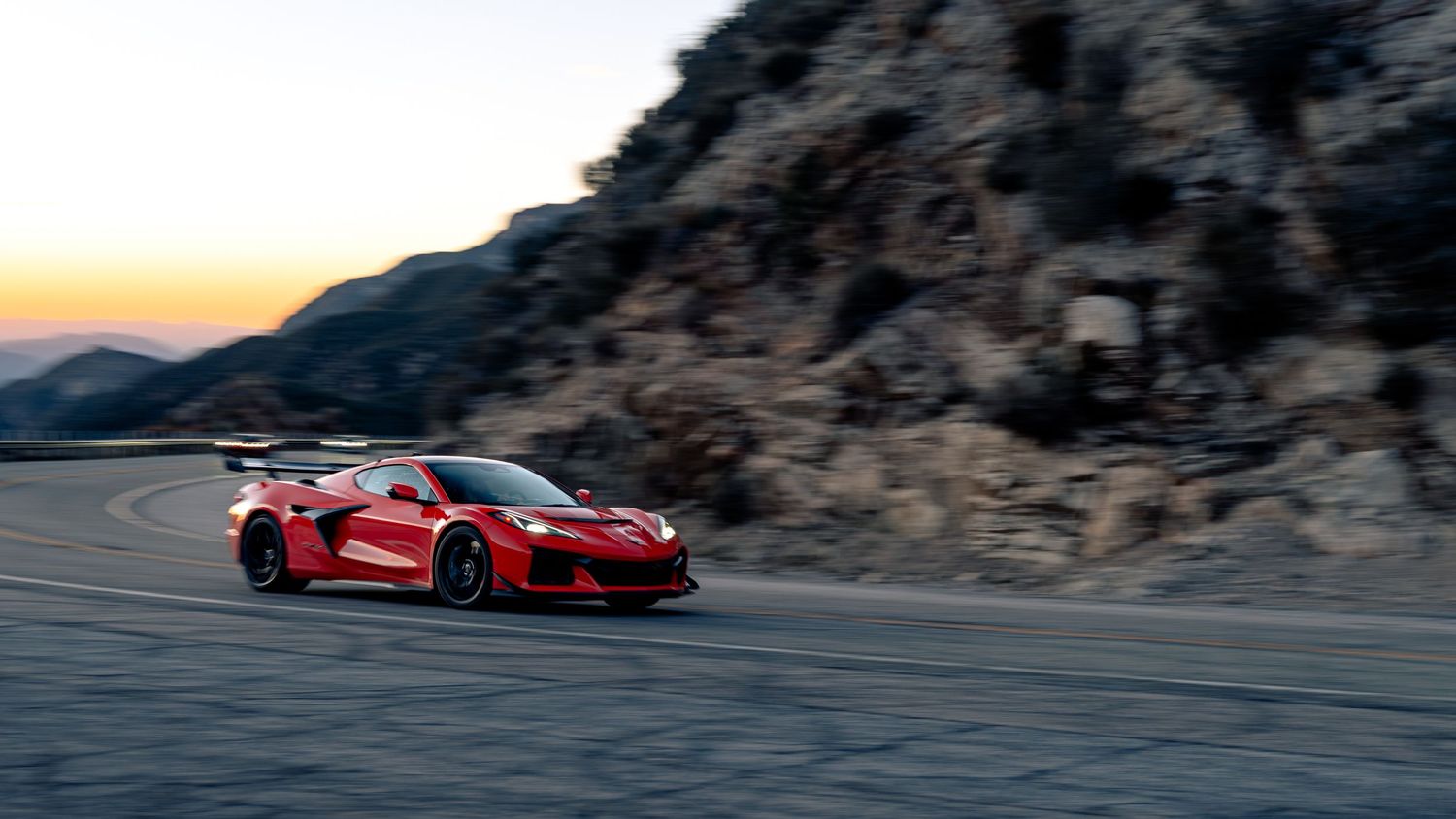 High-performance cars racing through mountain pass during sunset.