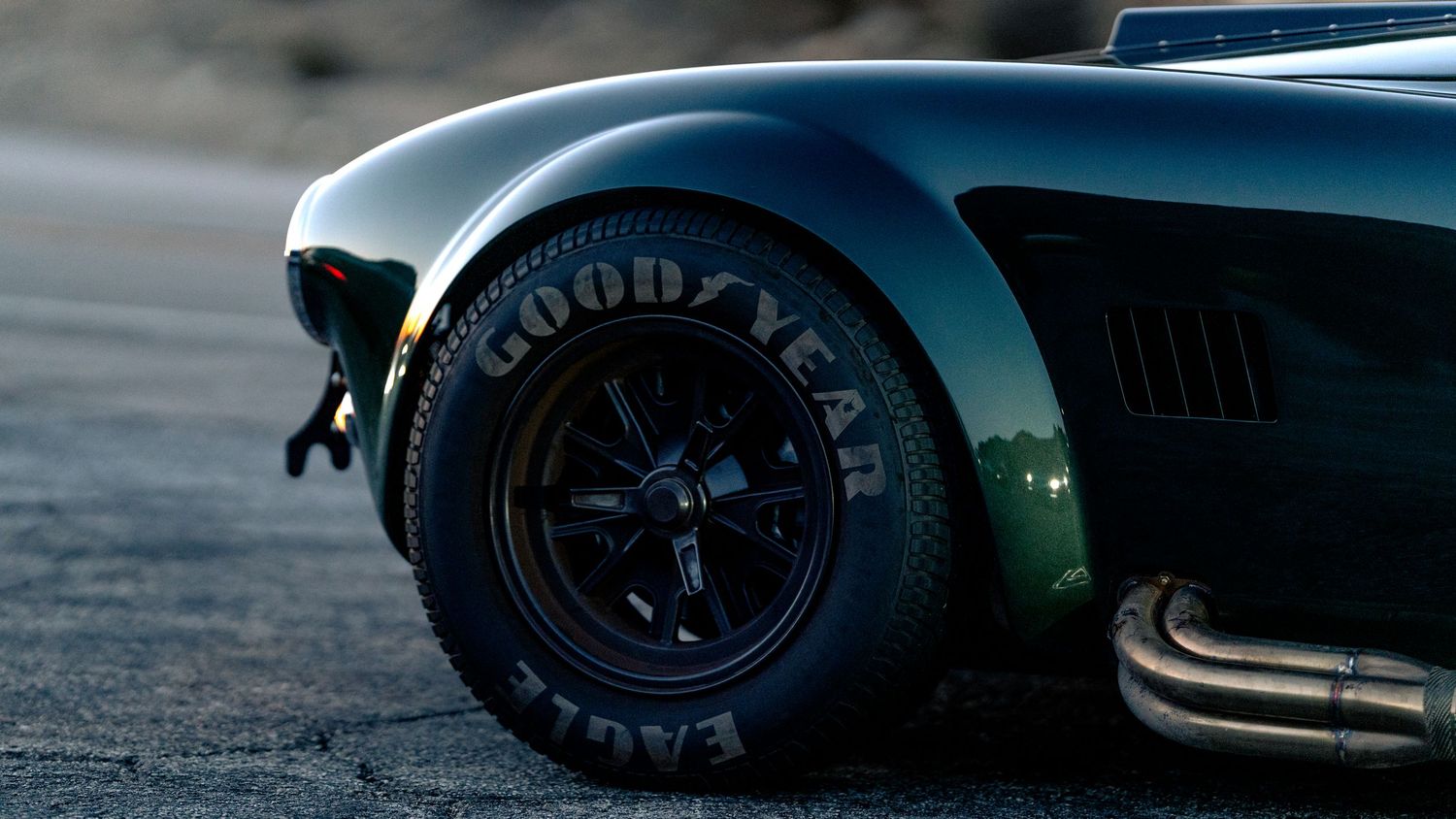 Close-up detail shot of a sports car wheel and tire on a mountain road at dusk.