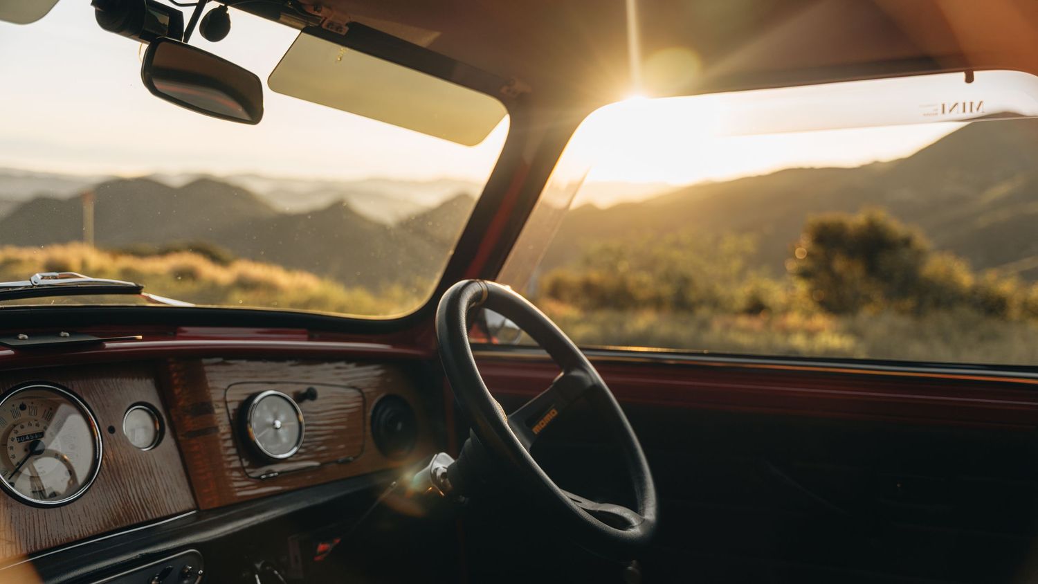 A collection of car interior dashboard views at sunset showing steering wheels and windshields with mountain scenery.