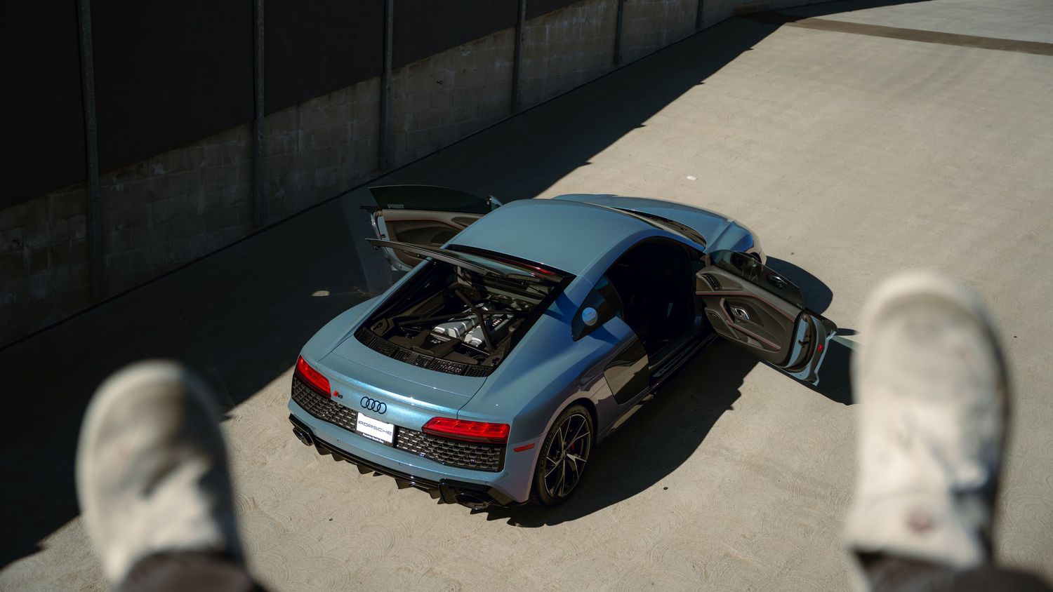 High angle view of a blue Audi R8 sports car with open door on concrete surface.