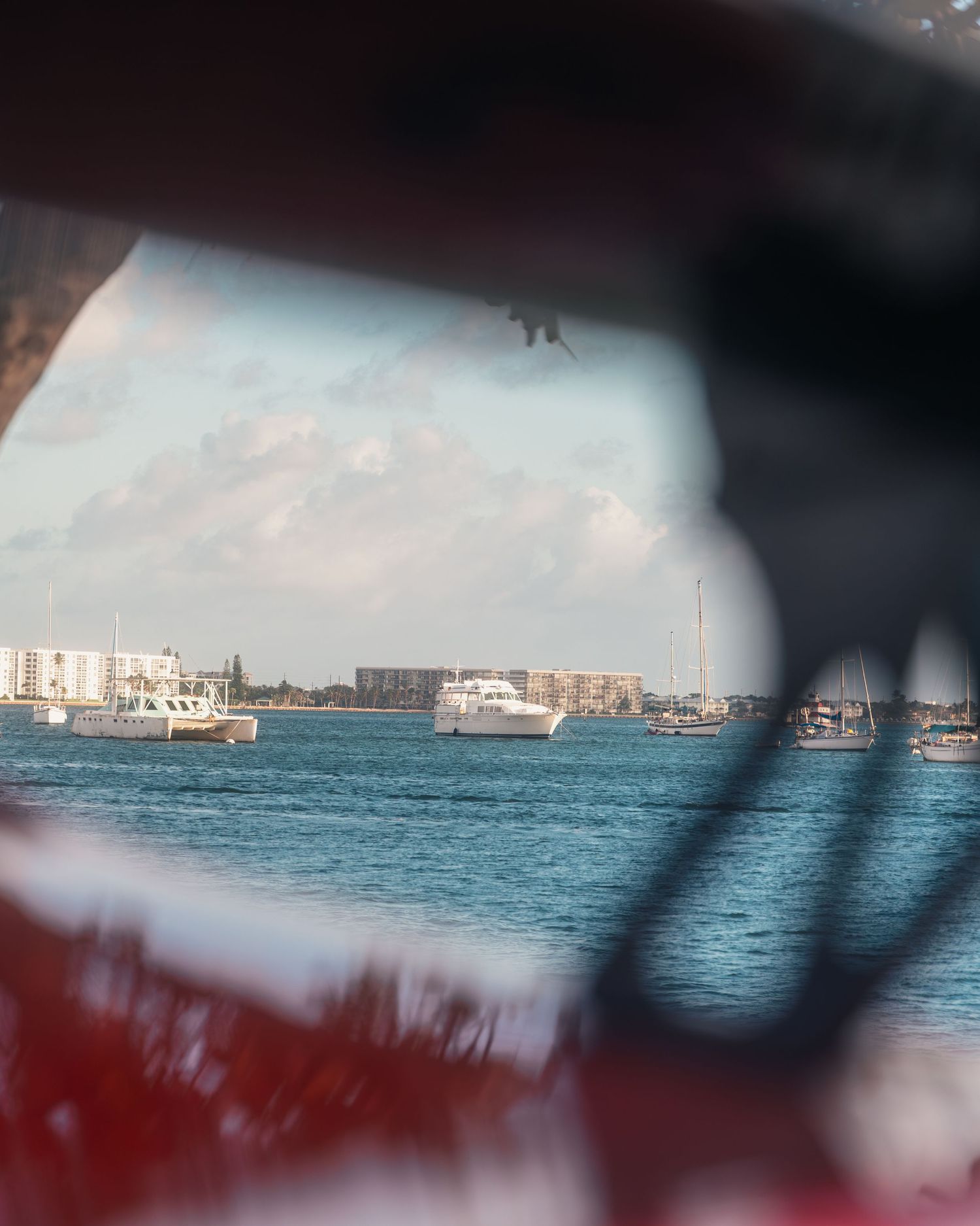 View through boat frame of calm harbor waters with white boats and city skyline under partly cloudy skies.