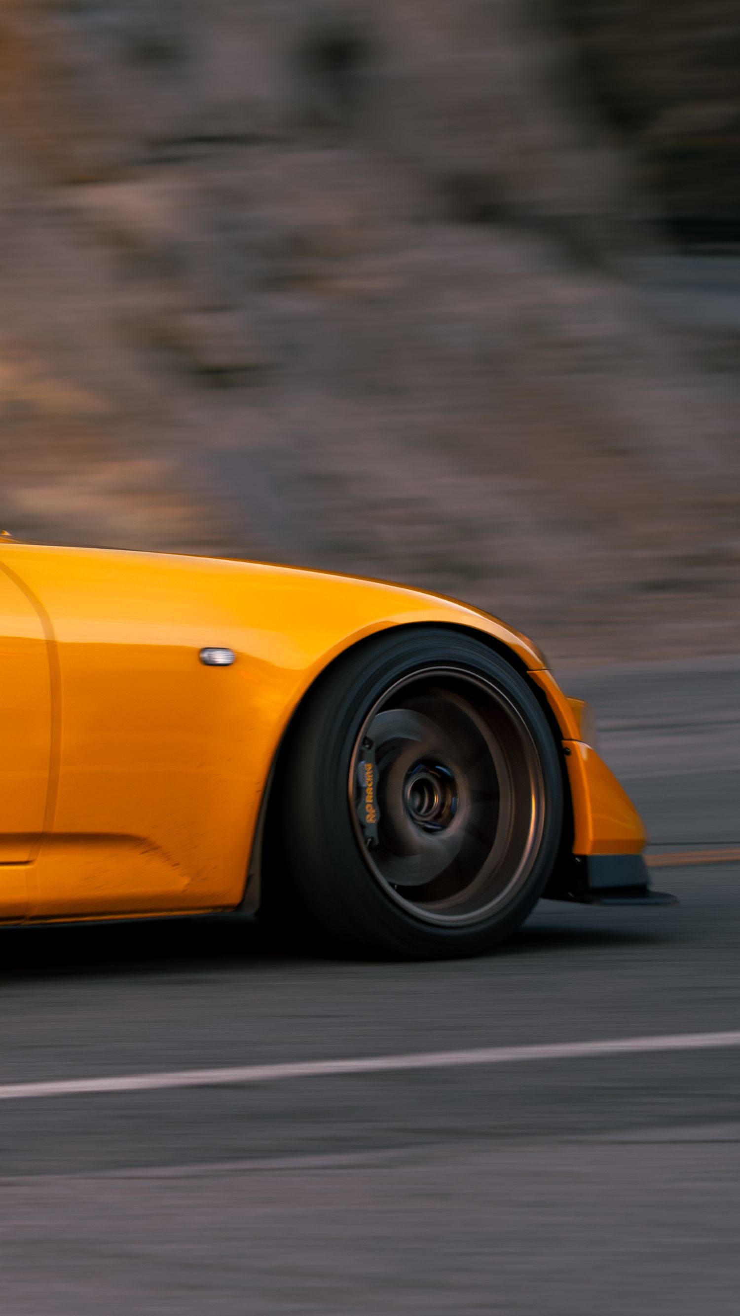 Close-up motion shot of an orange sports car's wheel and side panel.