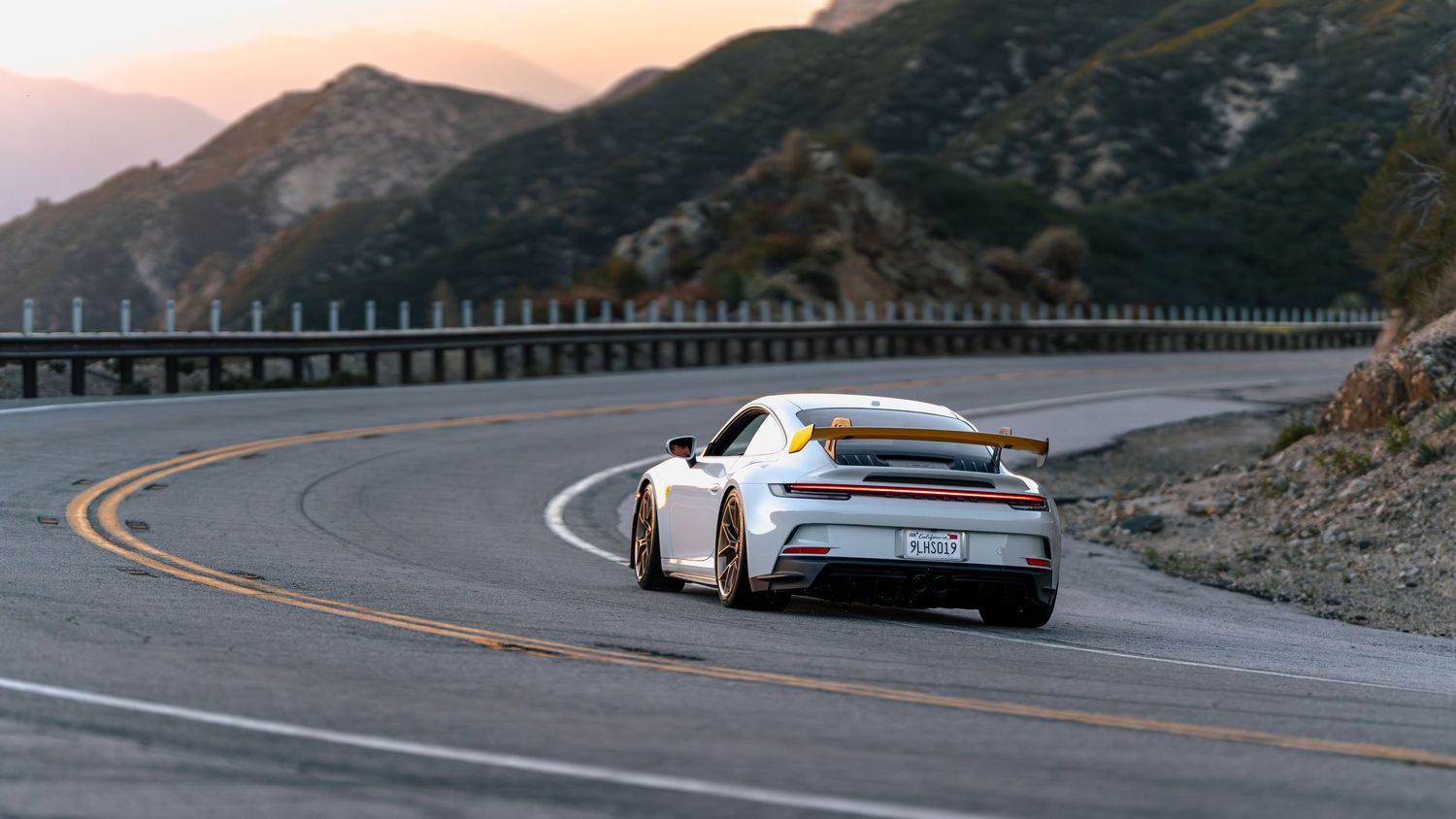 Panoramic view of mountain road with guard rails during golden hour.