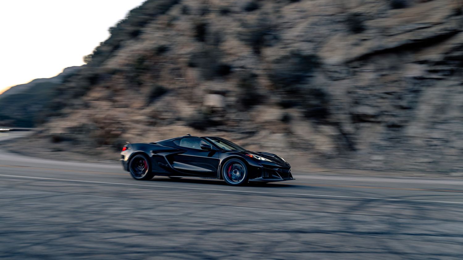 Performance vehicles driving through winding mountain pass at dusk.
