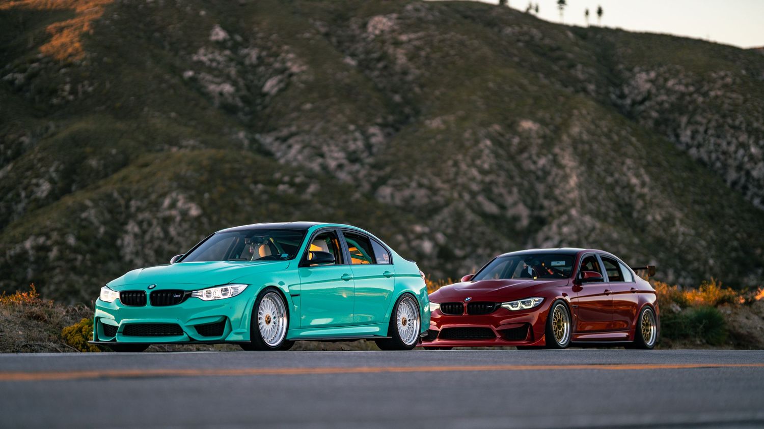 Wide panoramic view of BMW M3s driving on mountain roads during golden hour.